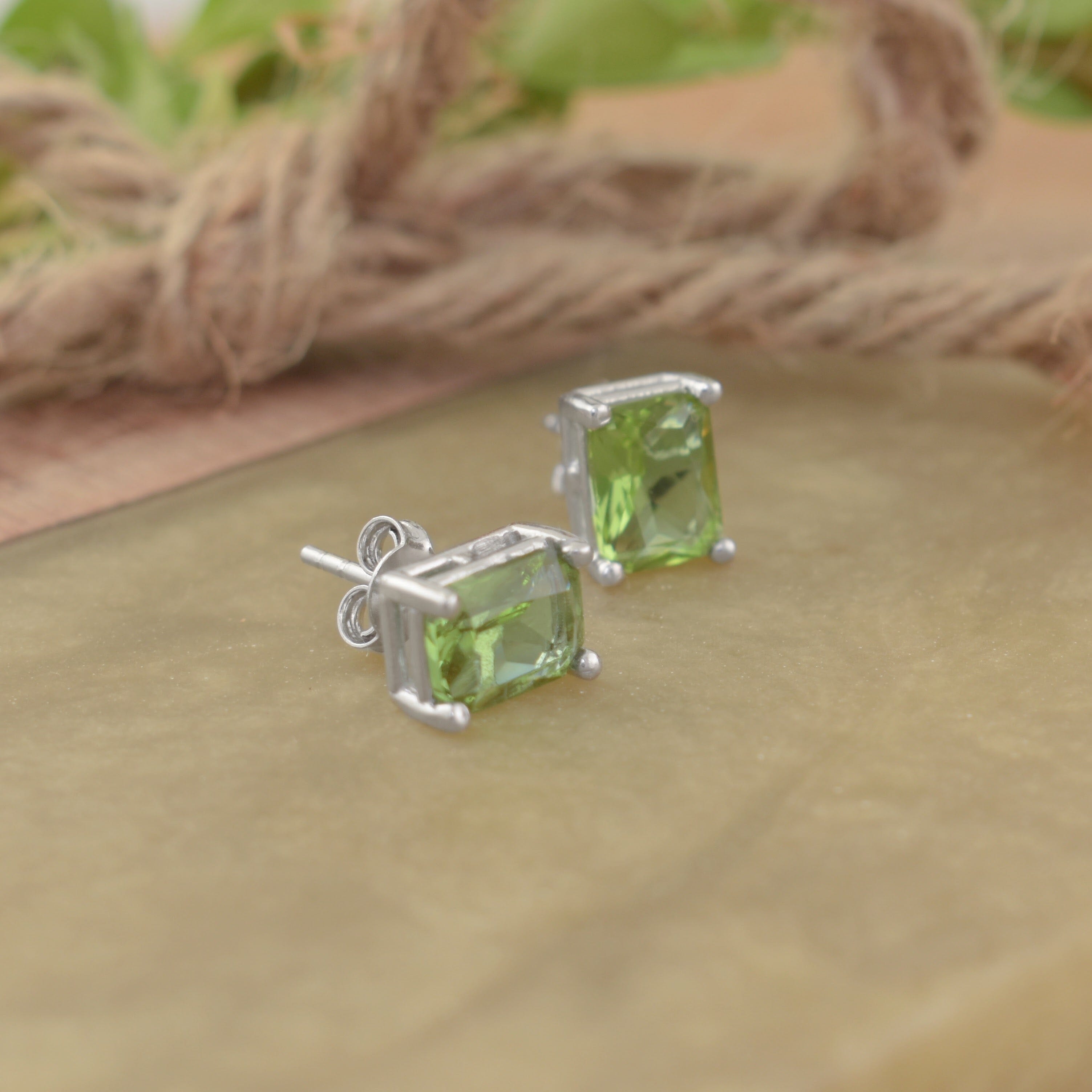A pair of stud earrings featuring an emerald cut light green stone