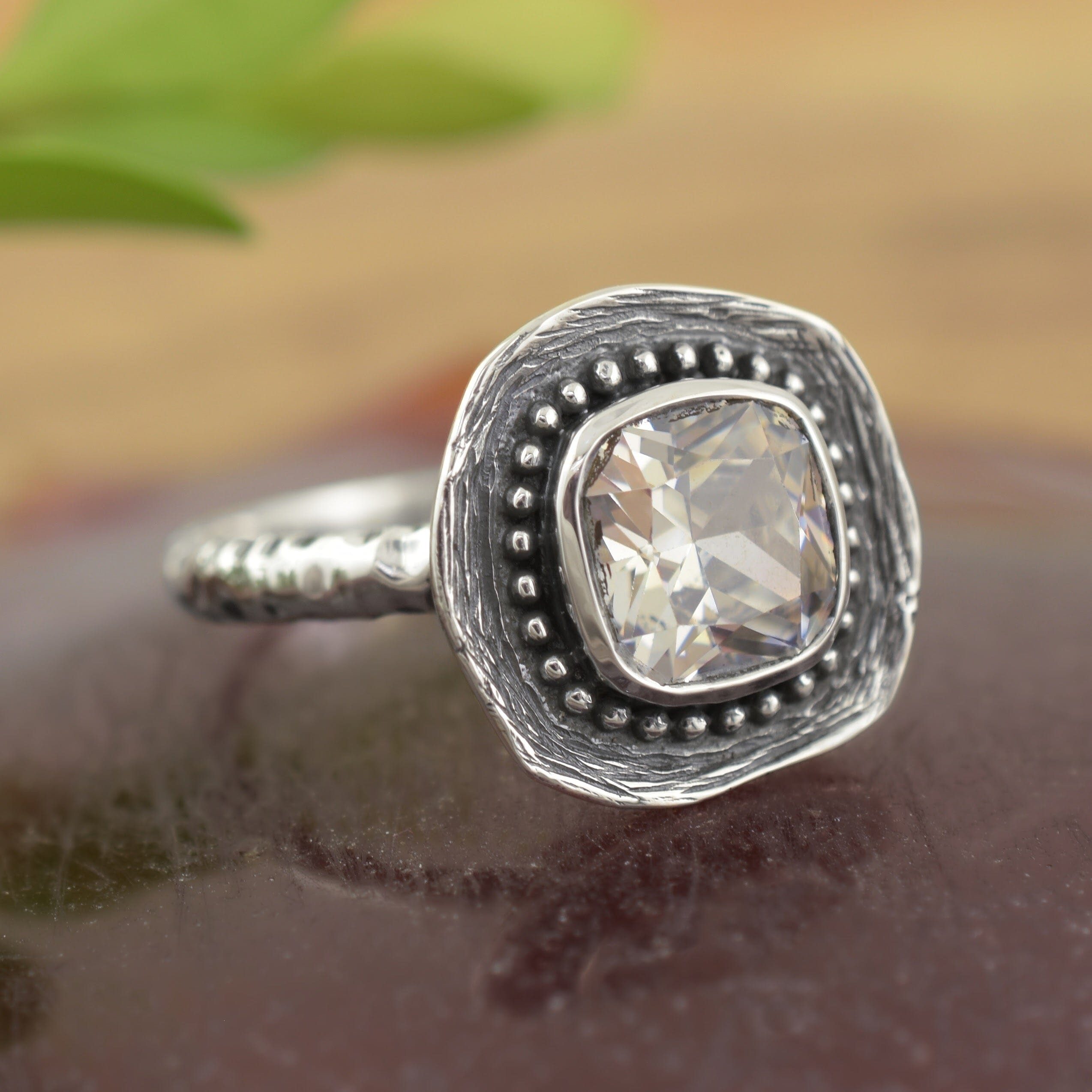A sterling silver ring, featuring a square cut clear CZ, with small silver beads framing the stone and a textured square base for it to sit on