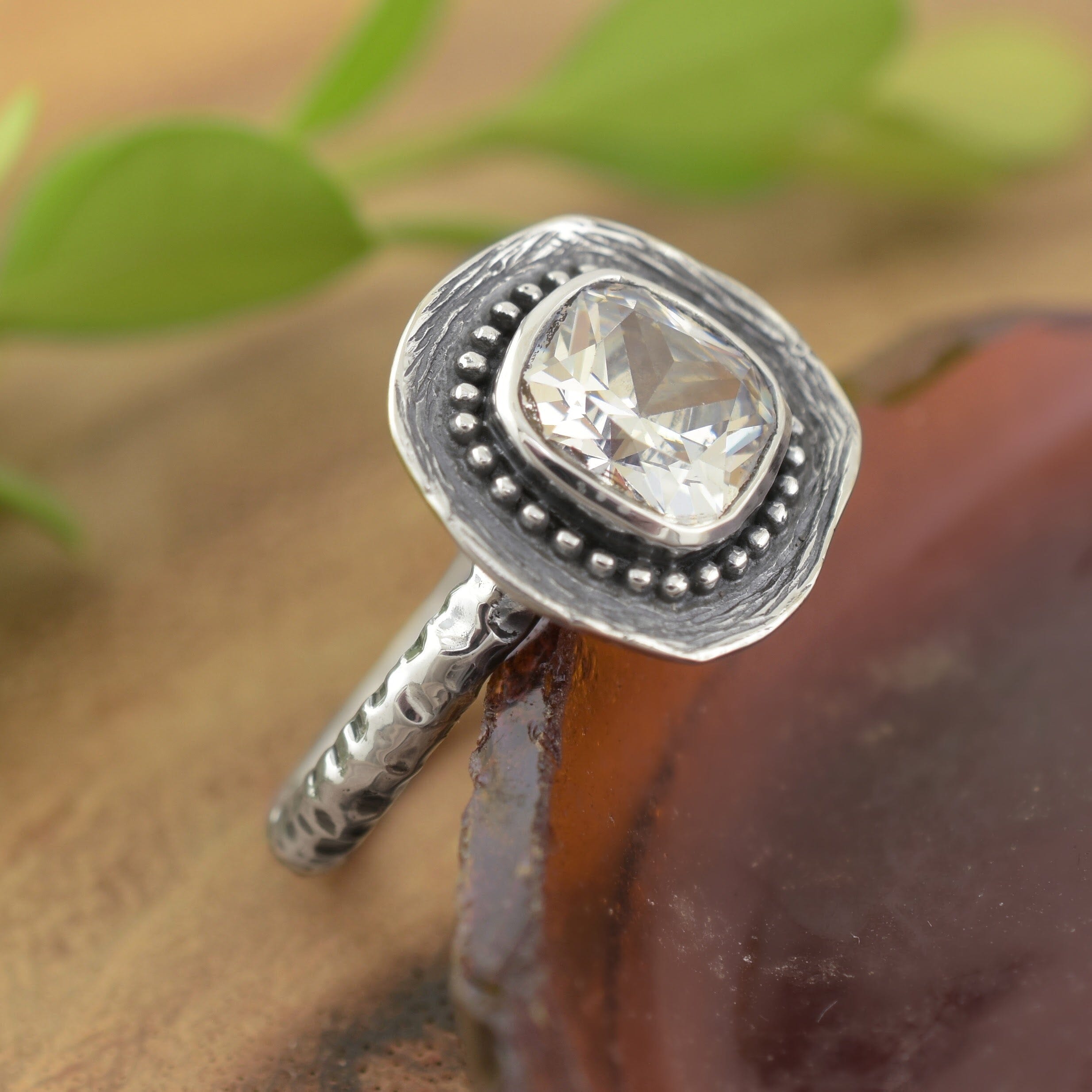 A sterling silver ring, featuring a square cut clear CZ, with small silver beads framing the stone and a textured square base for it to sit on