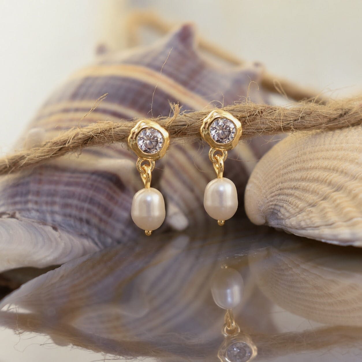 A pair of gold dangle earrings with clear round stones at the top and white baroque pearls hanging below