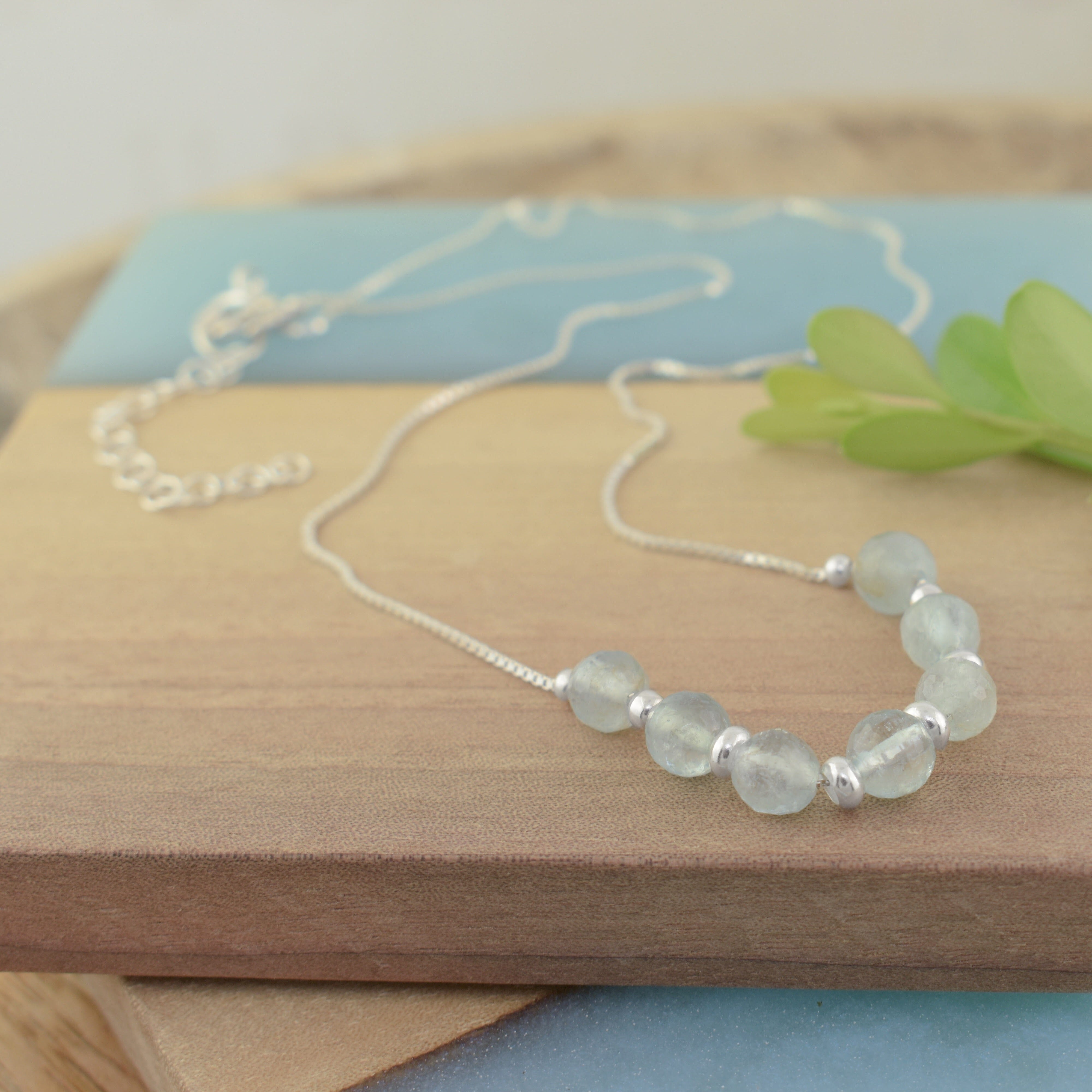 A sterling silver chain necklace with a row of translucent pale blue-green beads and small sterling silver spacer beads