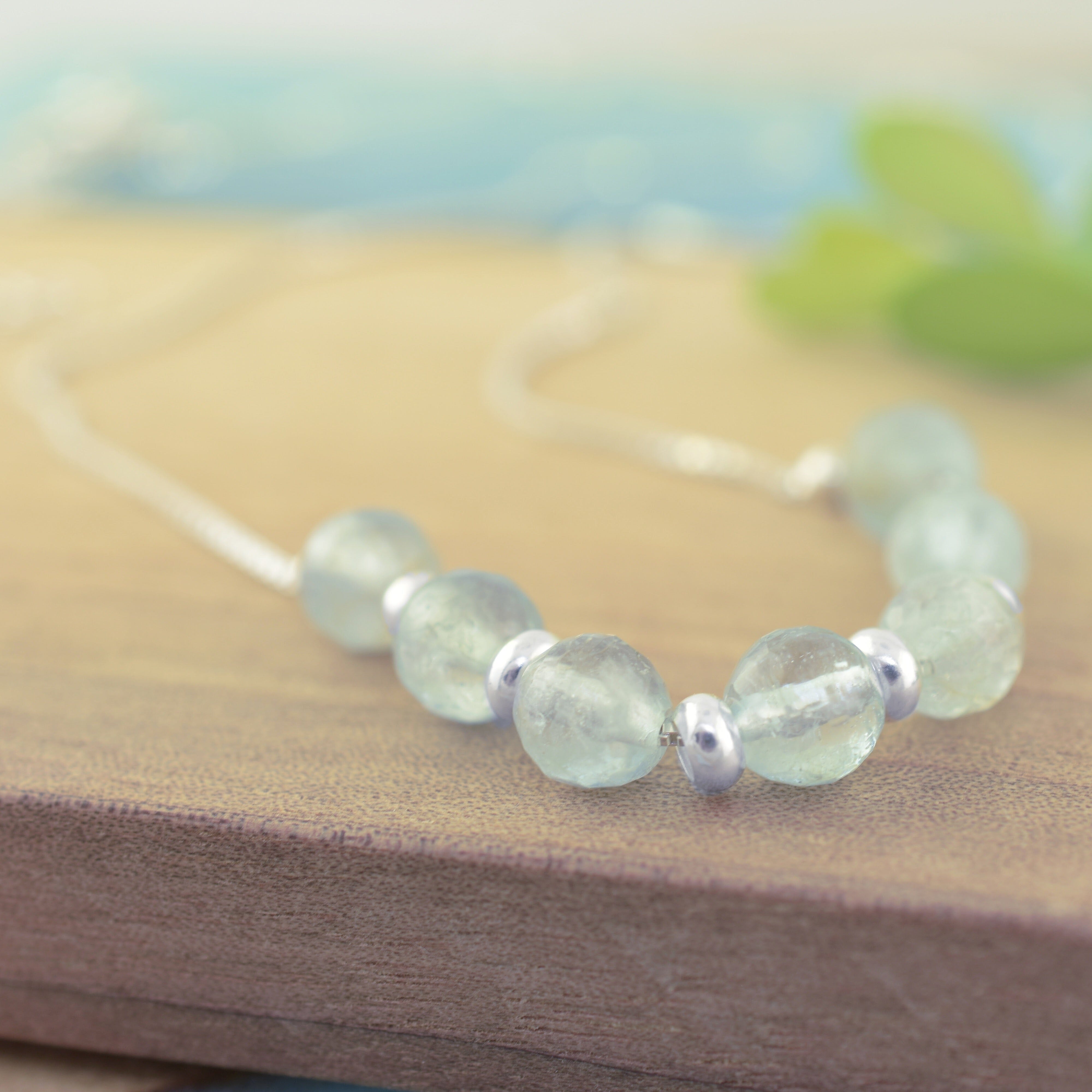 A close-up of a beaded necklace with light blue-green round beads and small sterling silver spacer beads