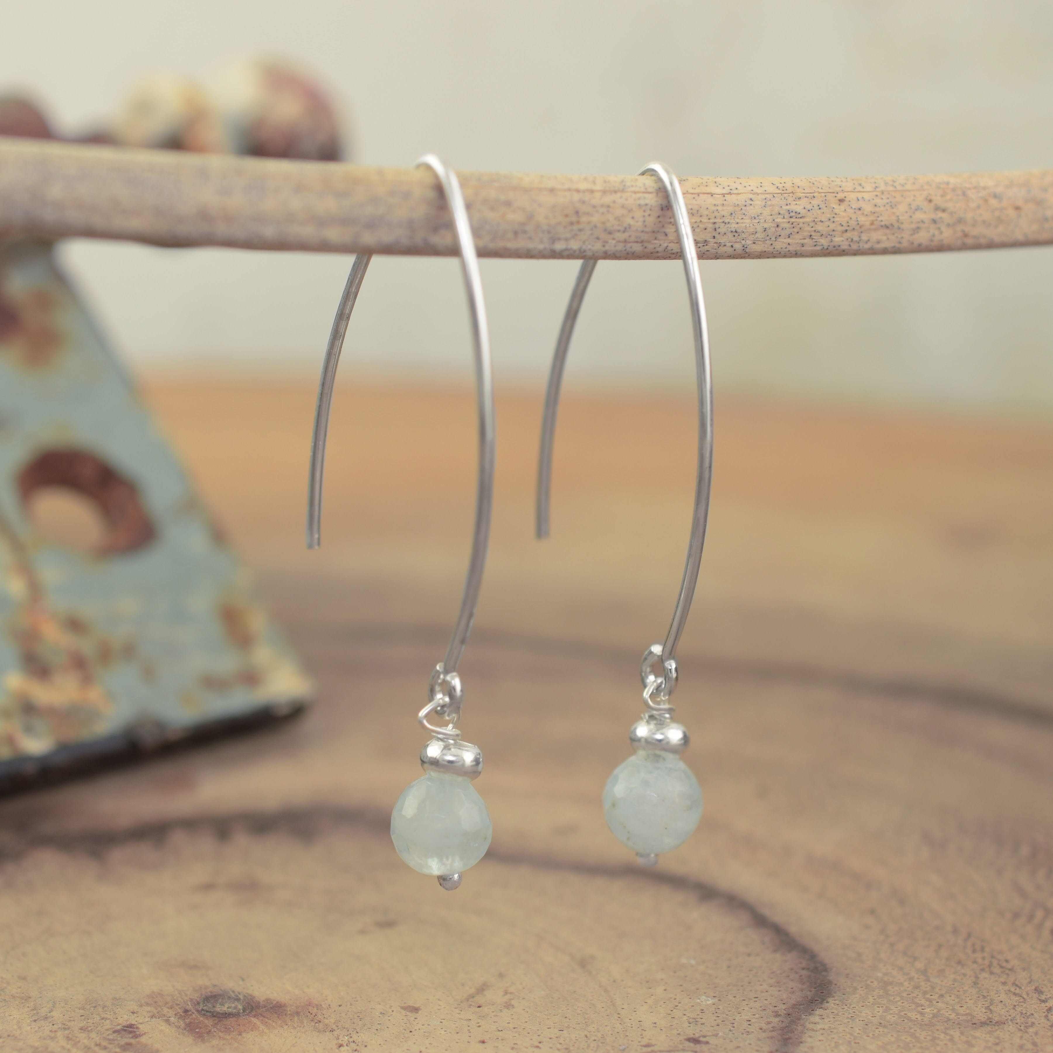 A pair of sterling silver hook earrings featuring an aquamarine bead dangling from the end