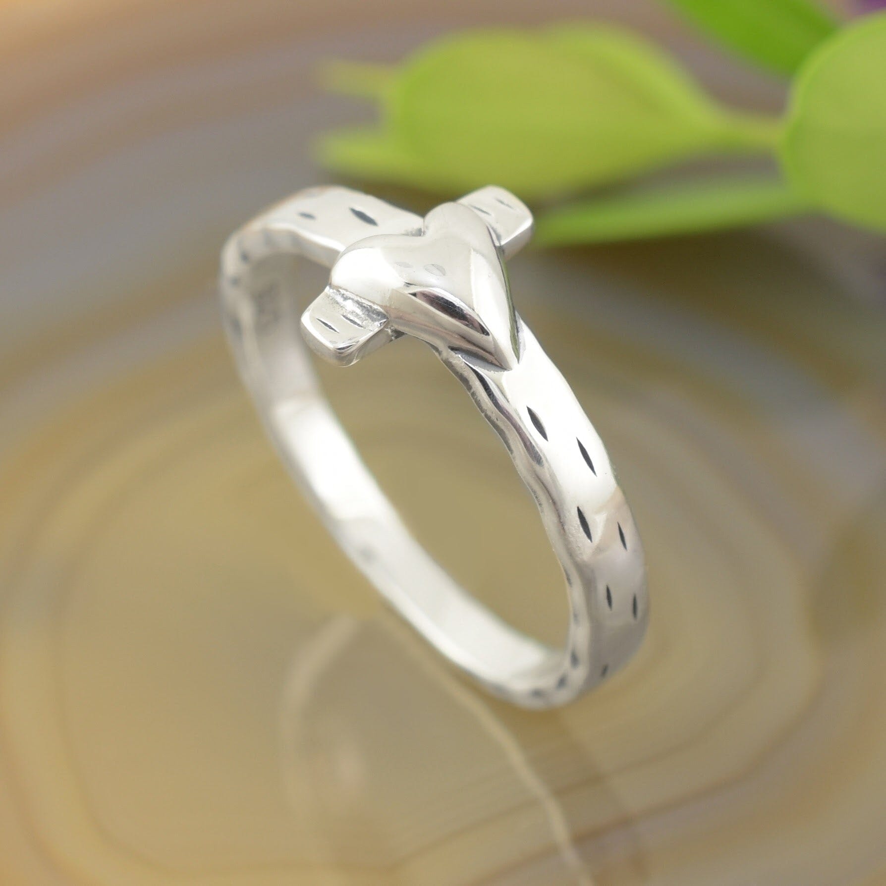 A sterling silver ring with a textured feel, featuring a cross with a small heart laying over top it