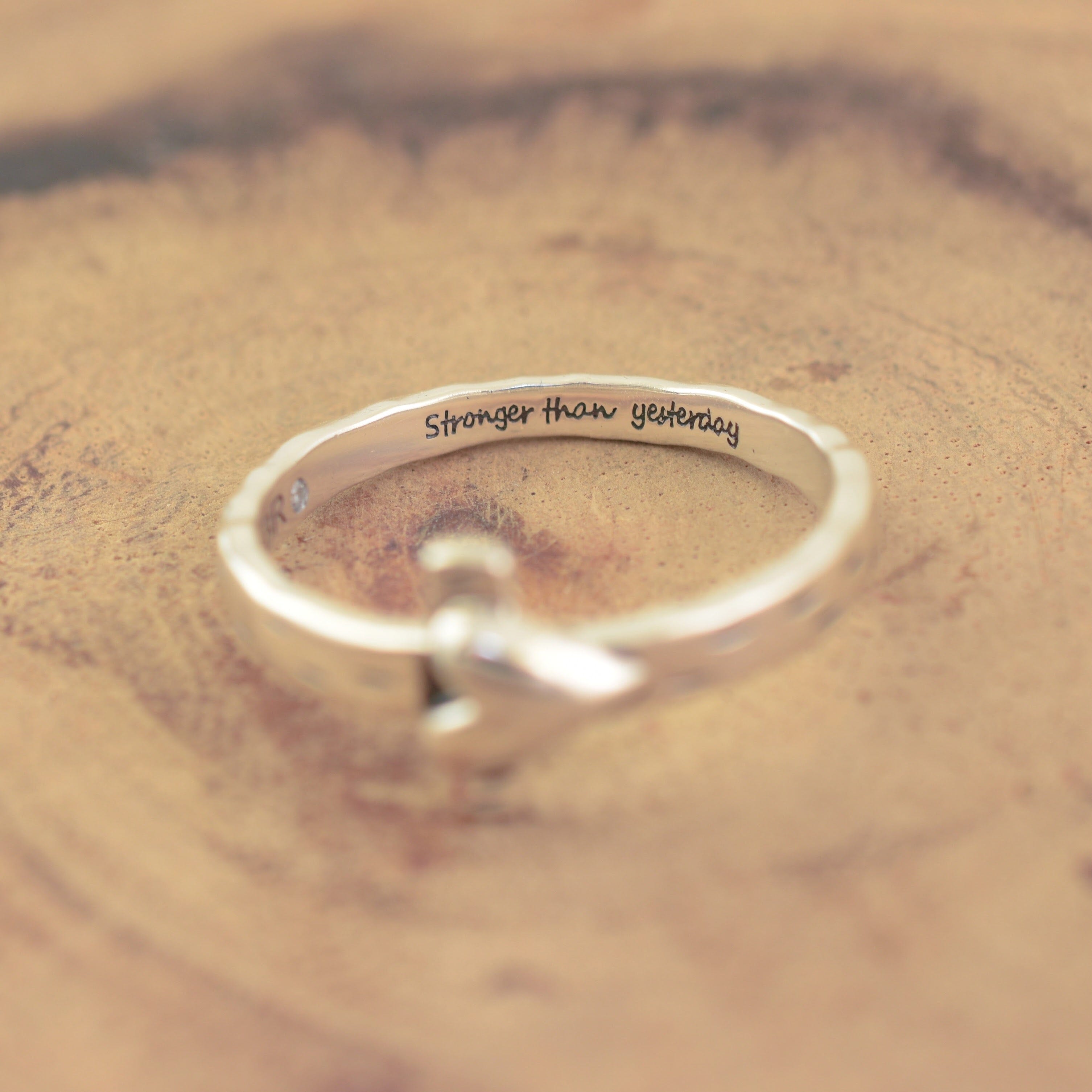 A sterling silver-plated brass band ring with a small heart over a cross detail and the engraved text 'Stronger than yesterday' on the inside