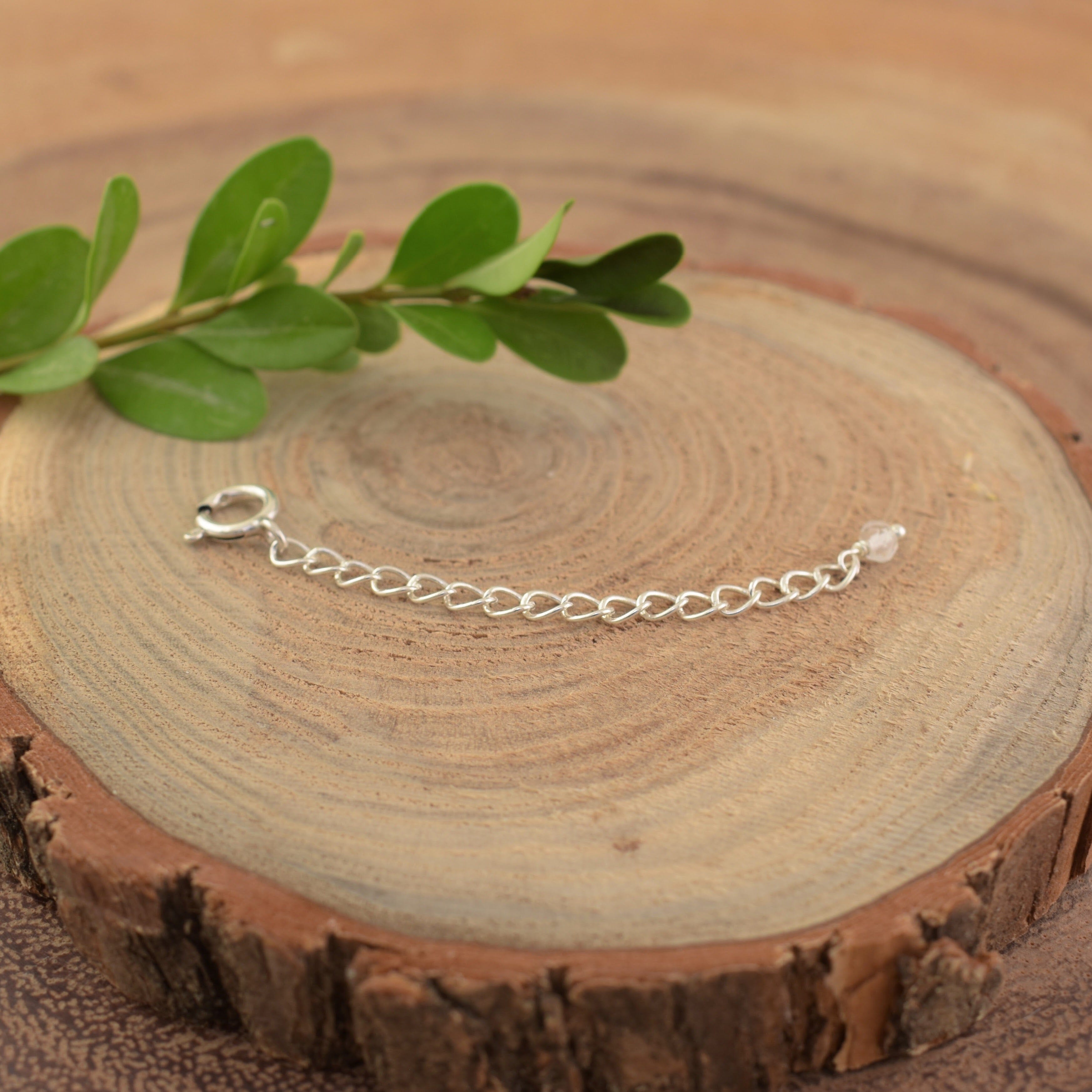 A sterling silver necklace extender with a spring ring closure on one end and a clear crystal on the other