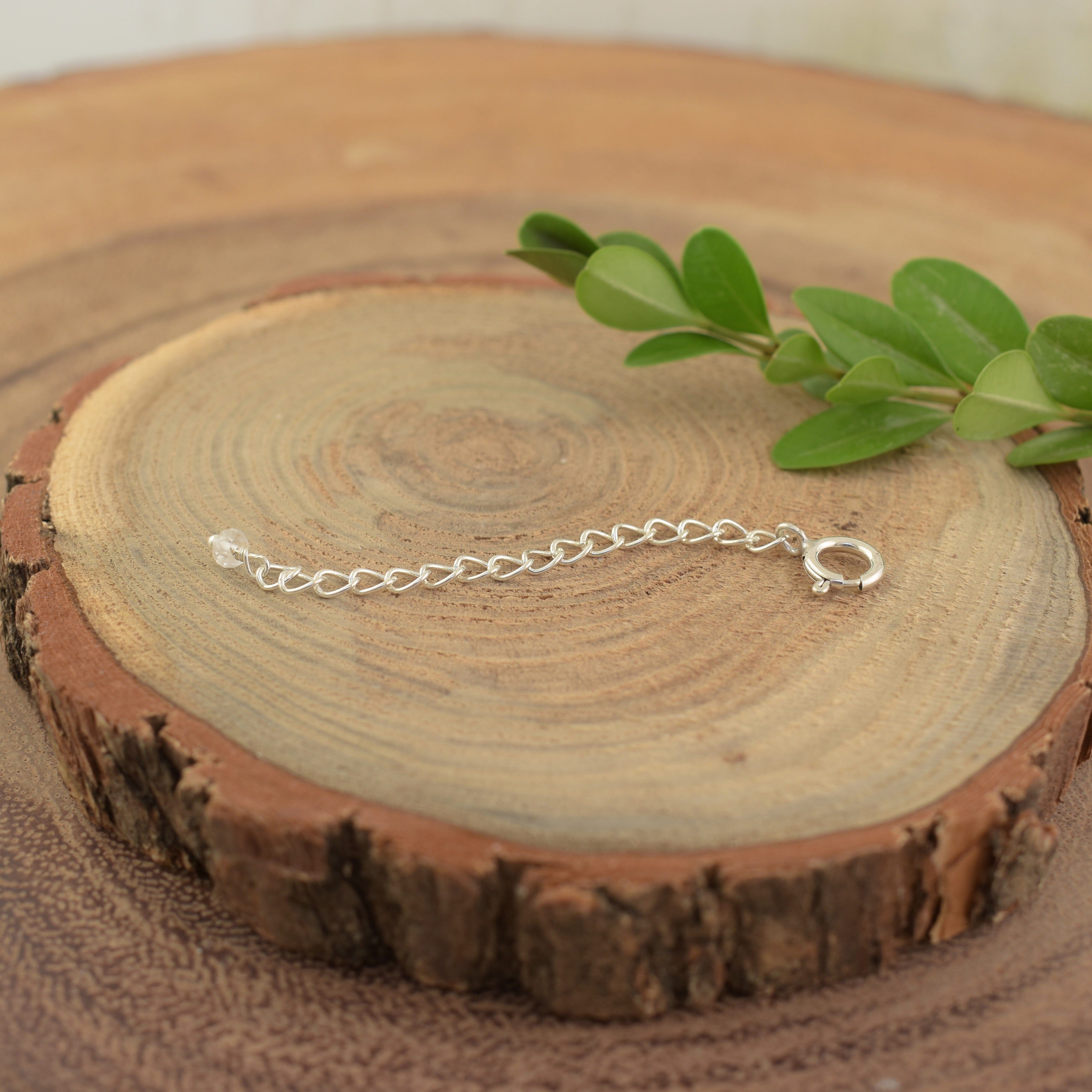 A sterling silver necklace extender with a spring ring closure on one end and a clear crystal on the other