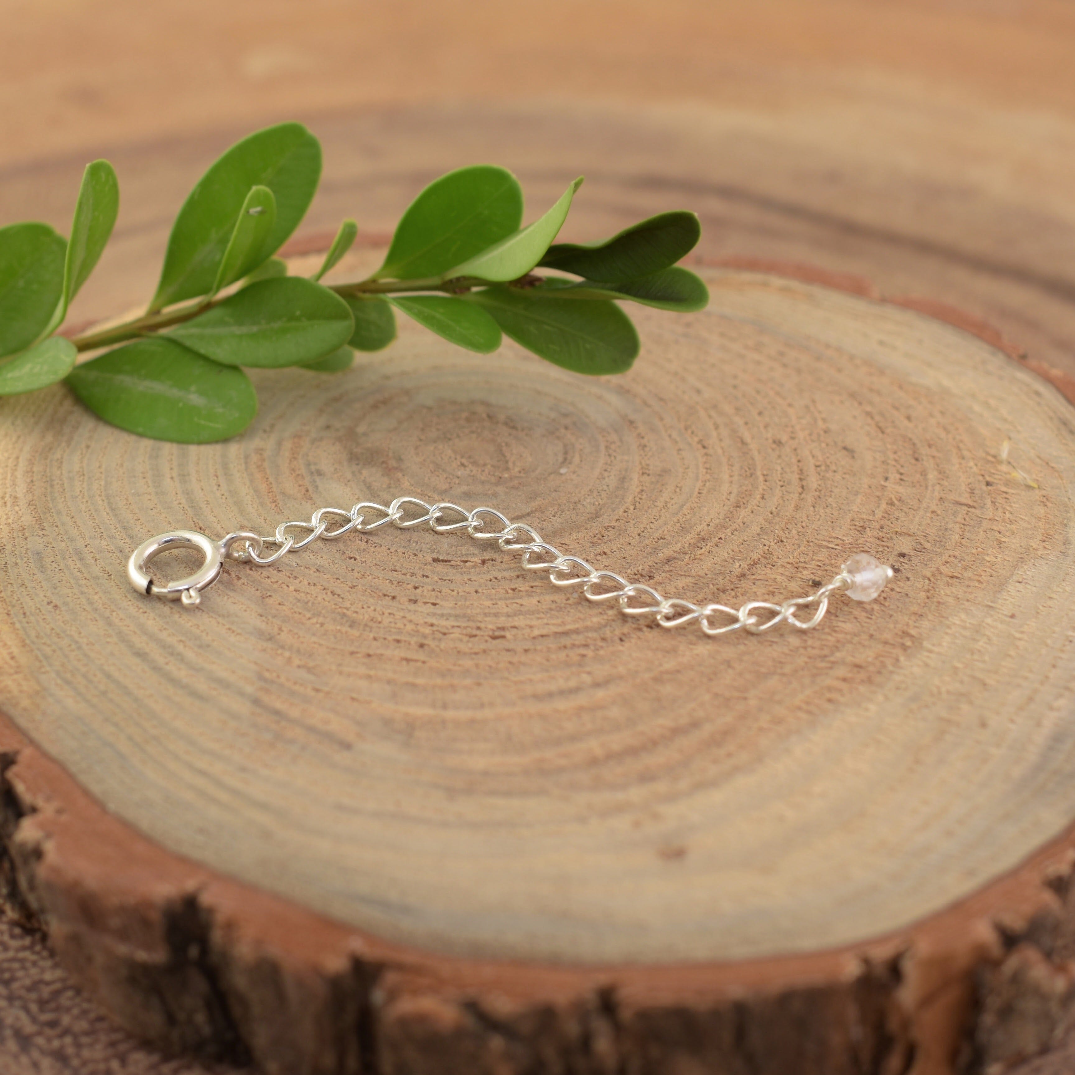 A sterling silver necklace extender with a spring ring closure on one end and a clear crystal on the other