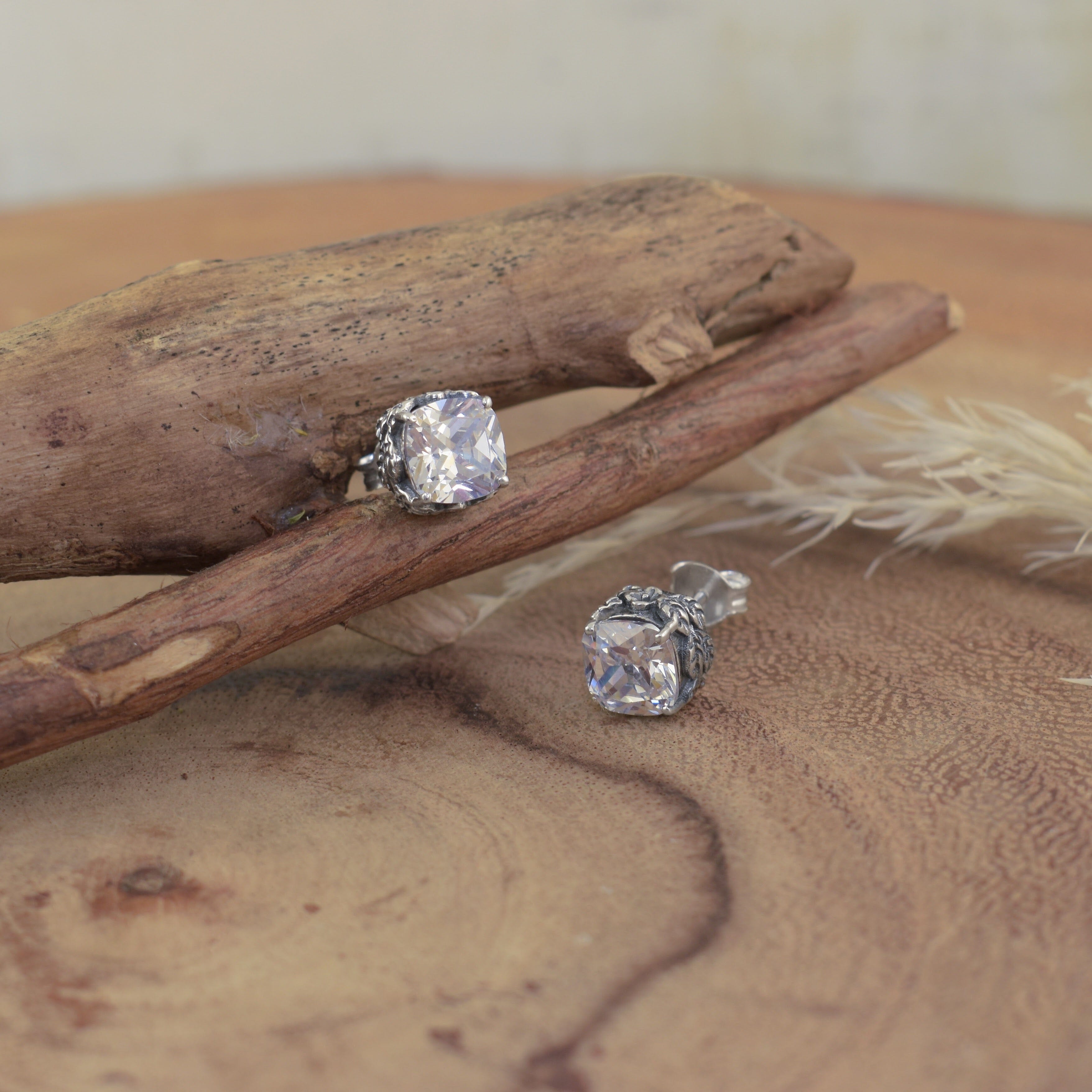 A pair of dainty sterling silver stud earrings, with a square-ish cut CZ stone and vine-like details along the sides