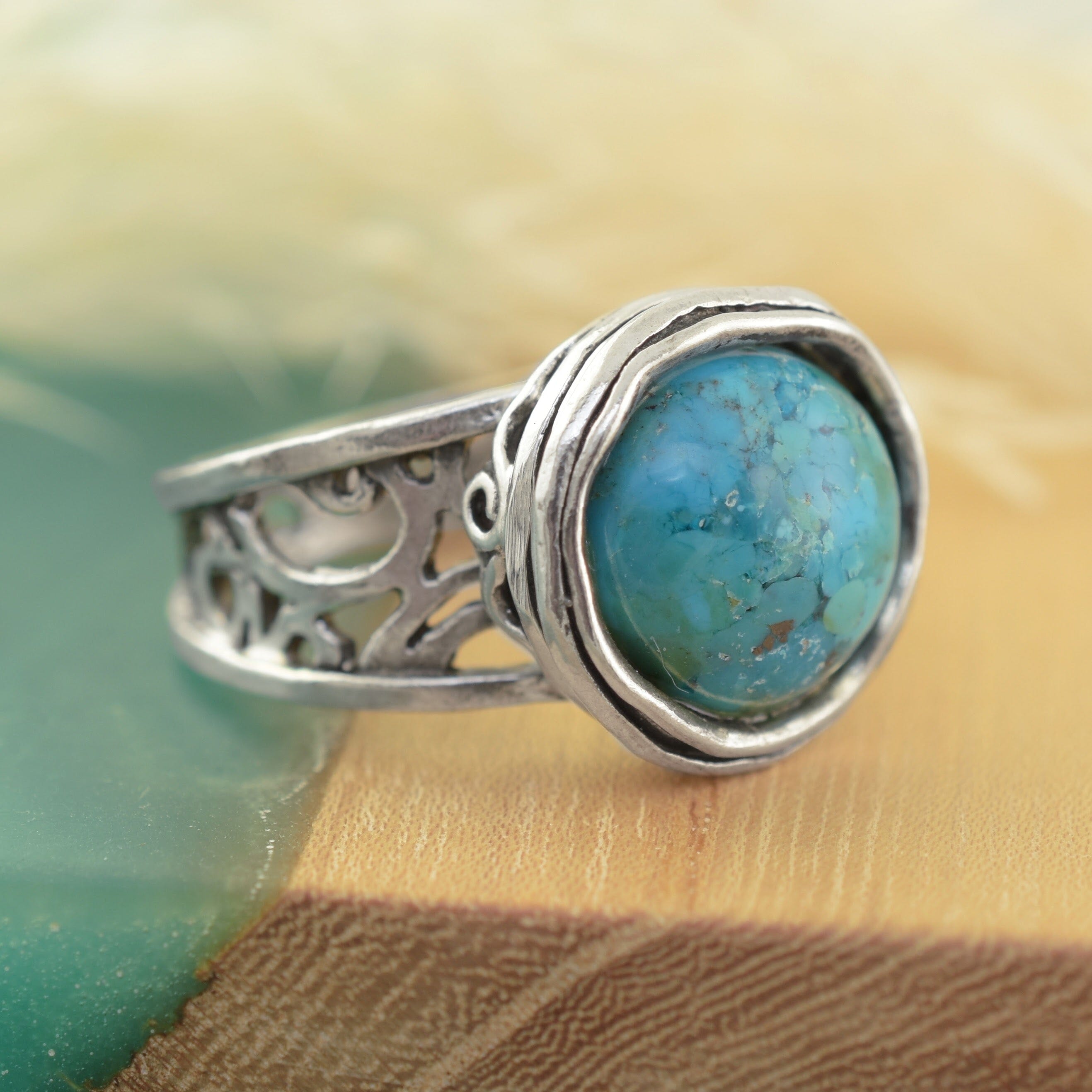 A sterling silver ring featuring a round turquoise-blue stone with natural matrix patterns, set in a textured bezel with an ornate filigree band