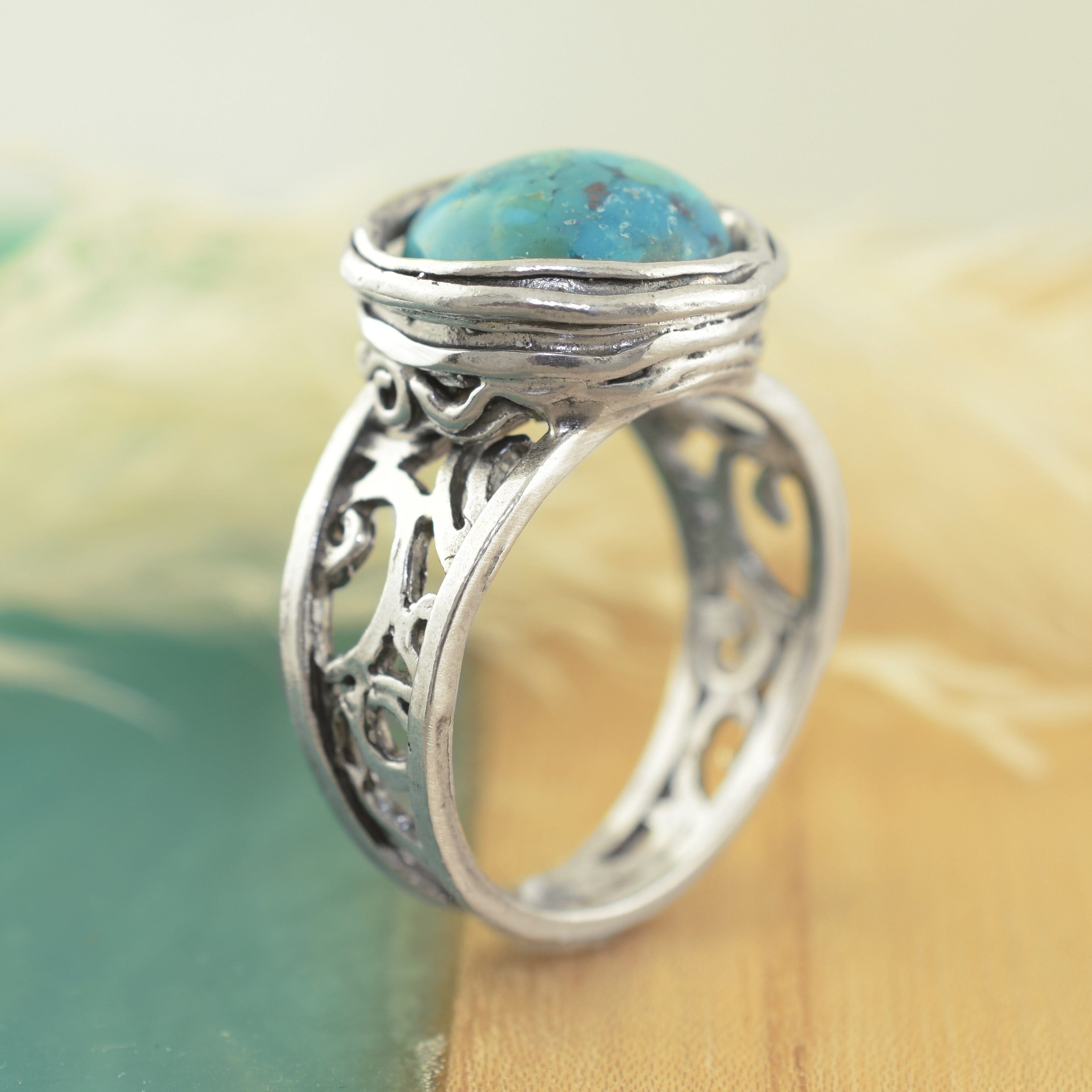 A sterling silver filigree ring featuring a round turquoise-blue stone in a textured bezel setting