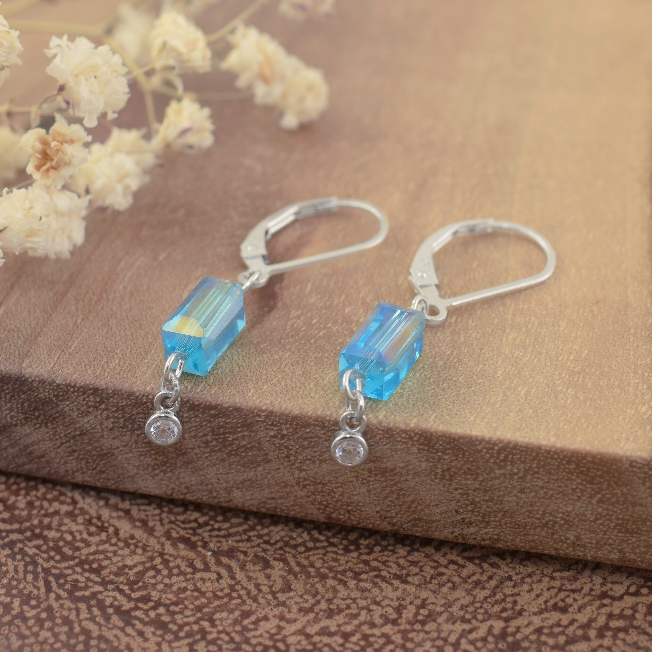 A pair of slingback sterling silver dangle earrings, featuring a rectangular aqua bead and a small round clear CZ stone hanging on the end
