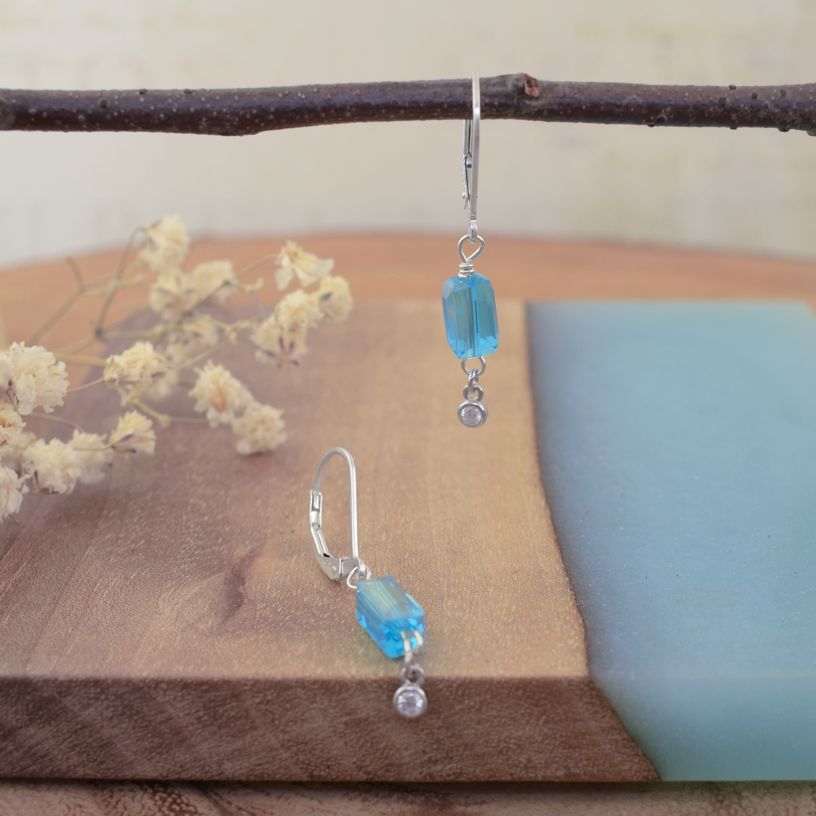 A pair of slingback sterling silver dangle earrings, featuring a rectangular aqua bead and a small round clear CZ stone hanging on the end