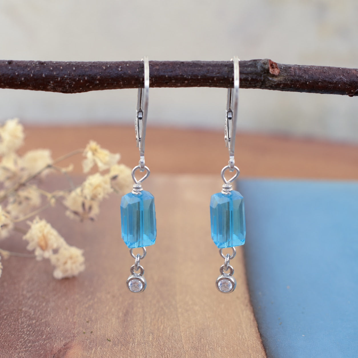 A pair of slingback sterling silver dangle earrings, featuring a rectangular aqua bead and a small round clear CZ stone hanging on the end