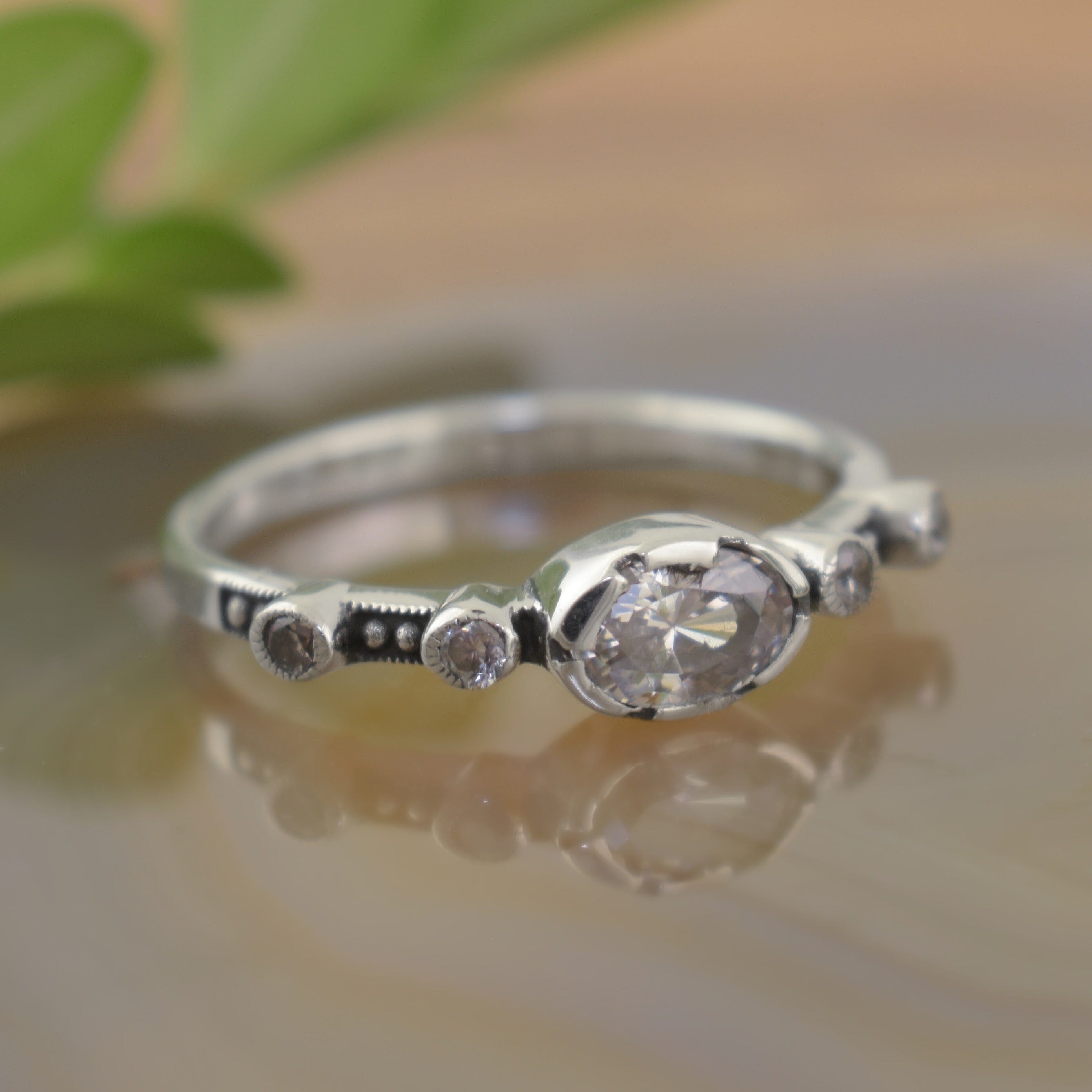 A sterling silver ring with a clear oval CZ in the center, framed by two small CZ stones on either side along the band