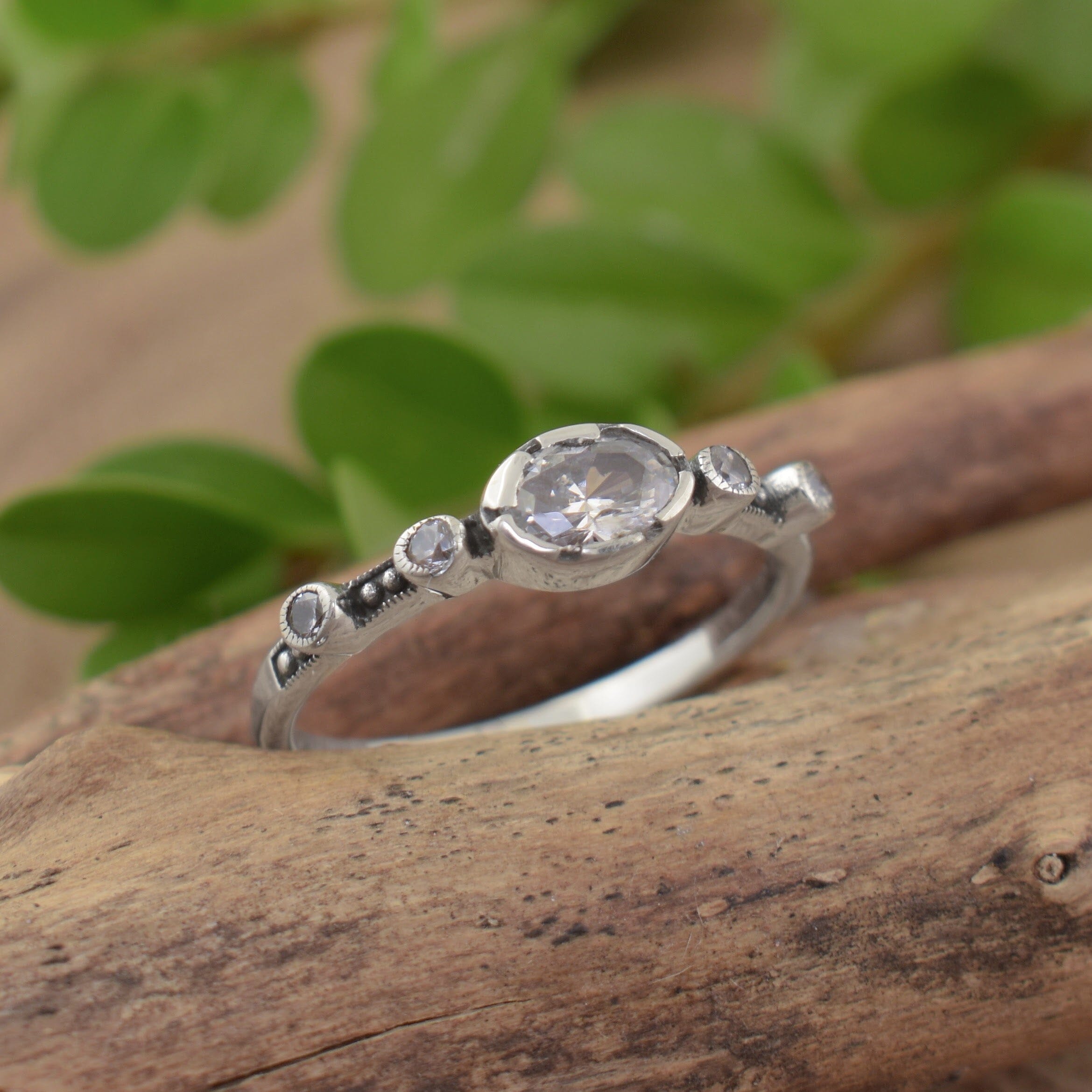 A small sterling silver ring featuring a clear oval CZ stone in the middle, framed on either side by two round CZ stones spaced along the band
