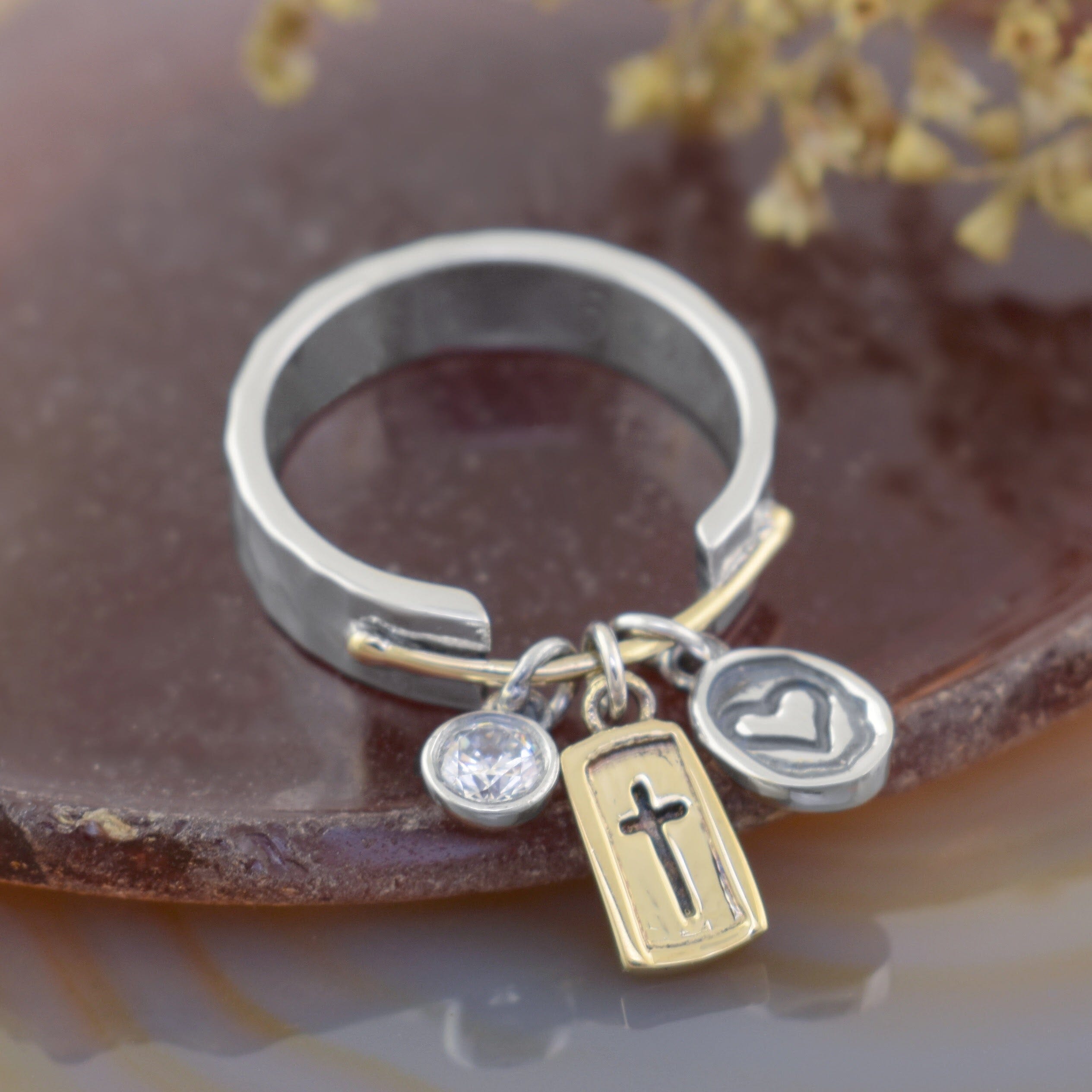 a silver and gold ring with three dangling charms: a clear round CZ stone, a gold-toned cross plaque, and a silver heart charm