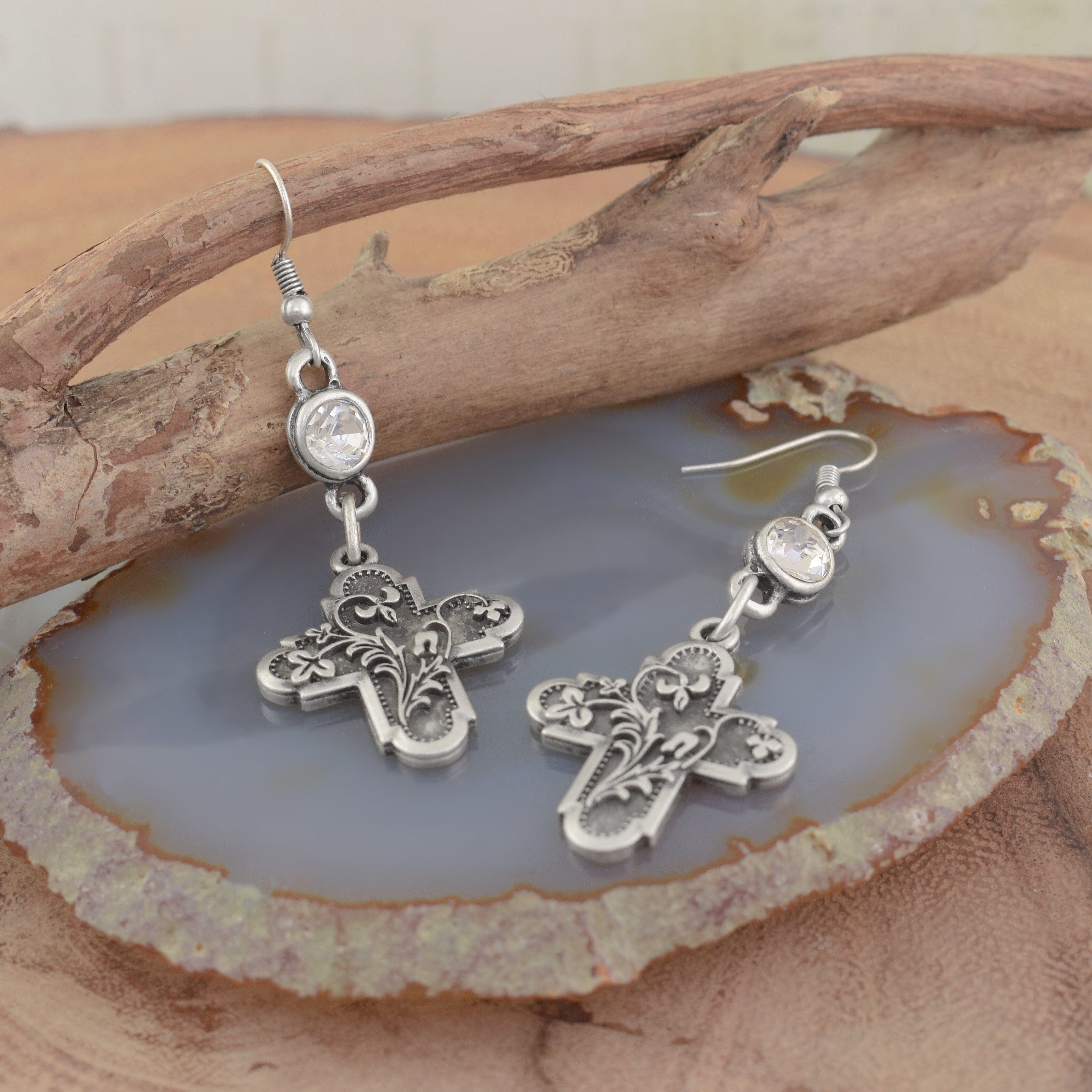 A pair of silver dangling earrings, featuring a round clear CZ and hanging beneath a filigree-engraved rustic cross pendant