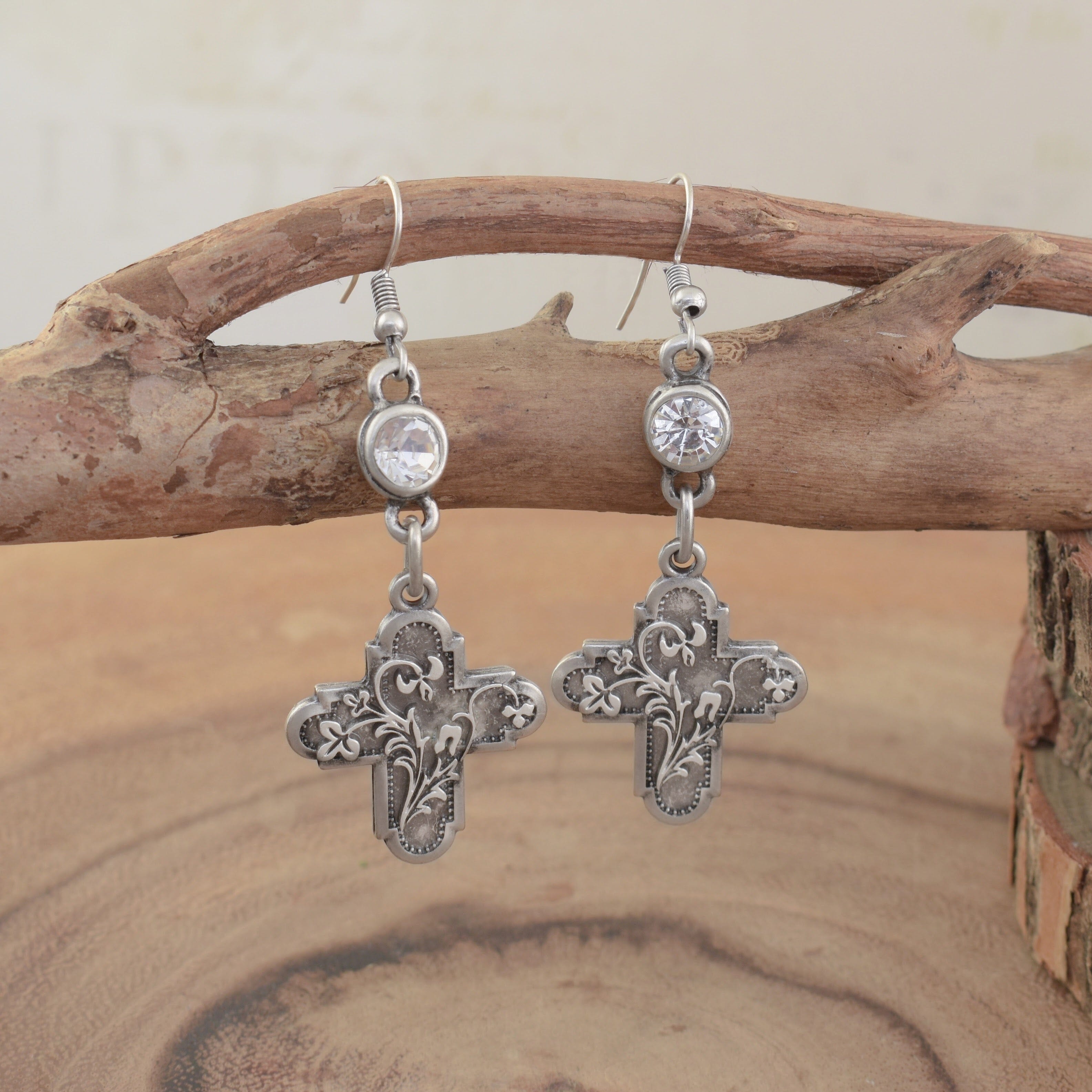 A pair of silver dangling earrings, featuring a round clear CZ and hanging beneath a filigree-engraved rustic cross pendant