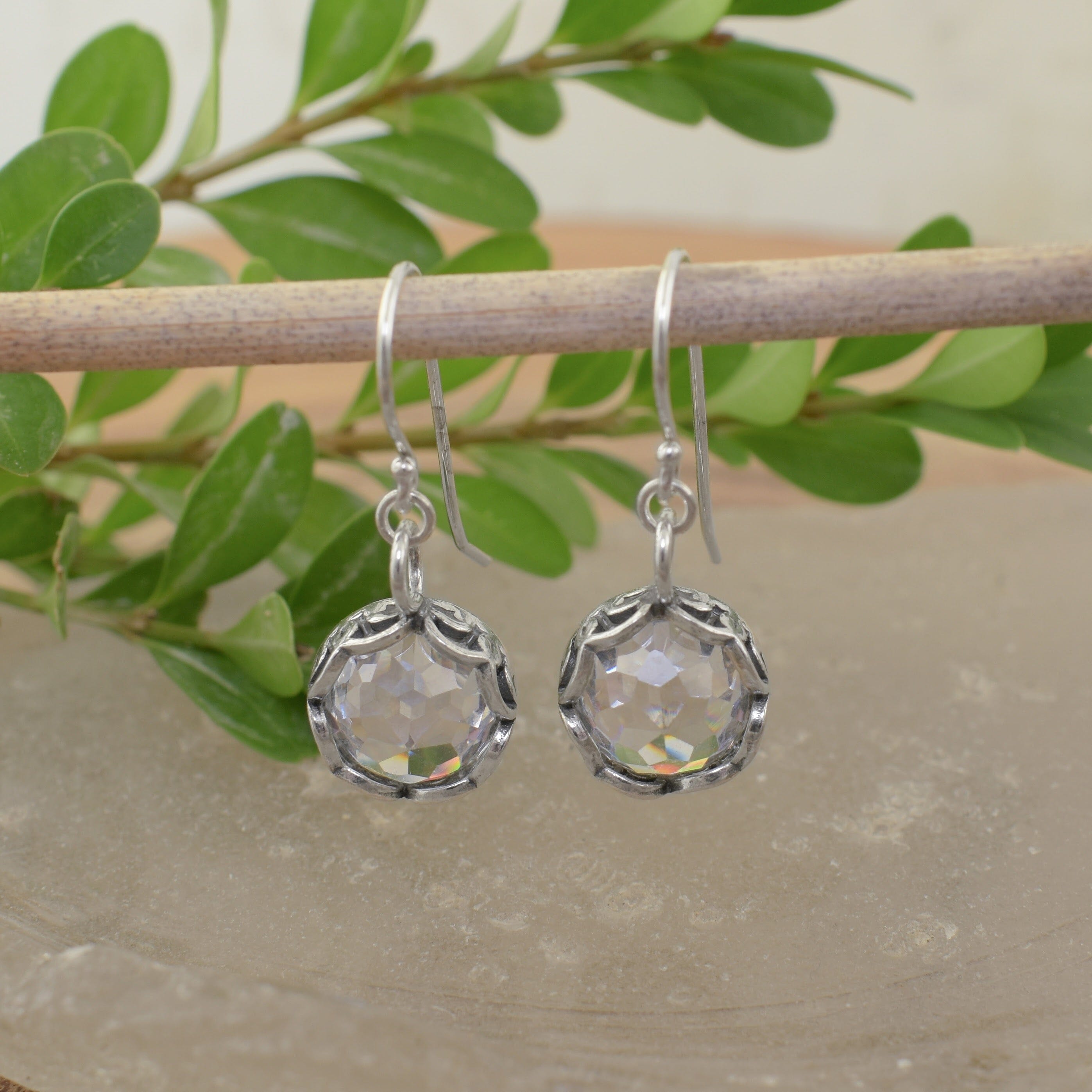 A pair of sterling silver earrings with french hooks and a dangling clear CZ stone with filigree details surrounding the stone