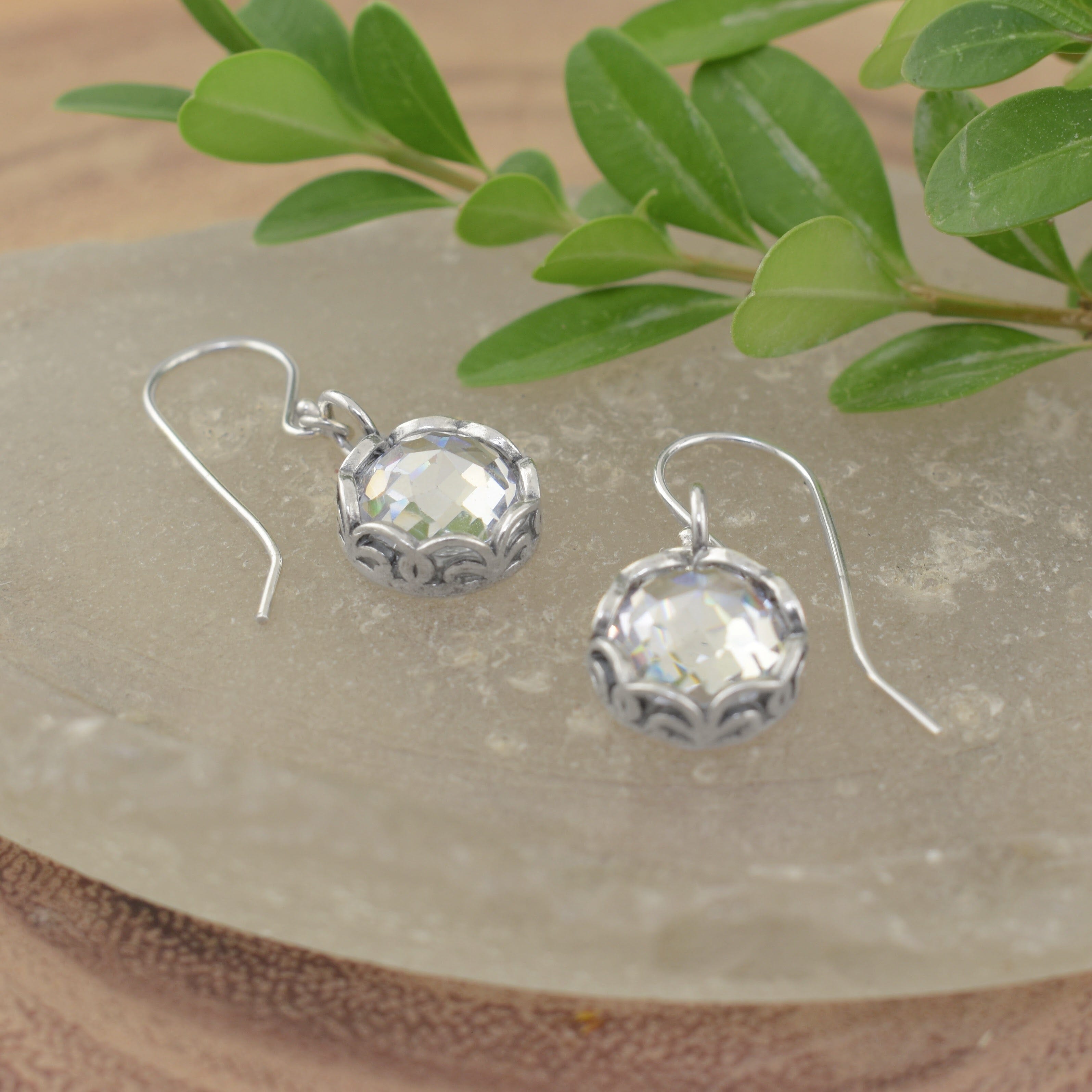 A pair of sterling silver earrings with french hooks and a dangling clear CZ stone with filigree details surrounding the stone
