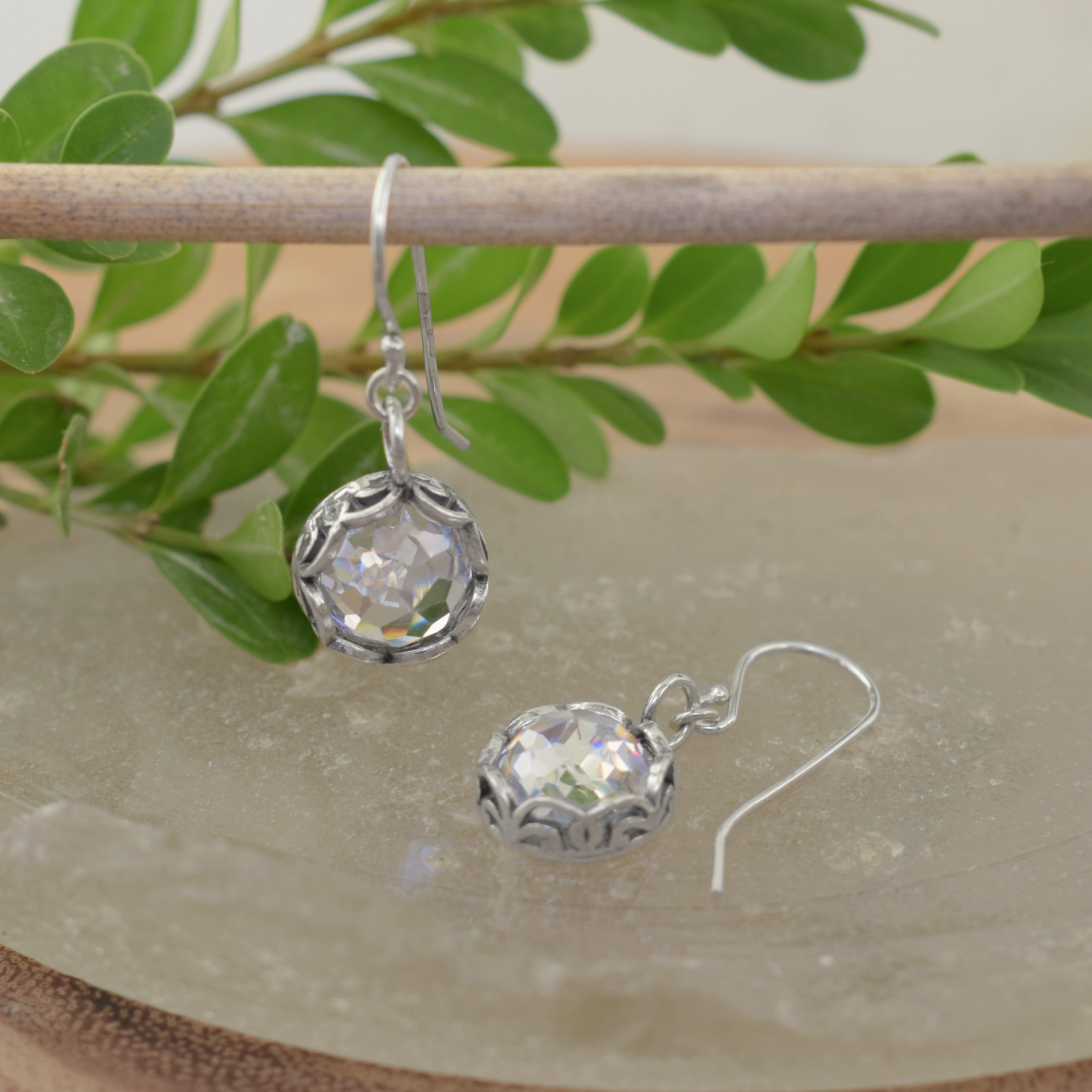 A pair of sterling silver earrings with french hooks and a dangling clear CZ stone with filigree details surrounding the stone