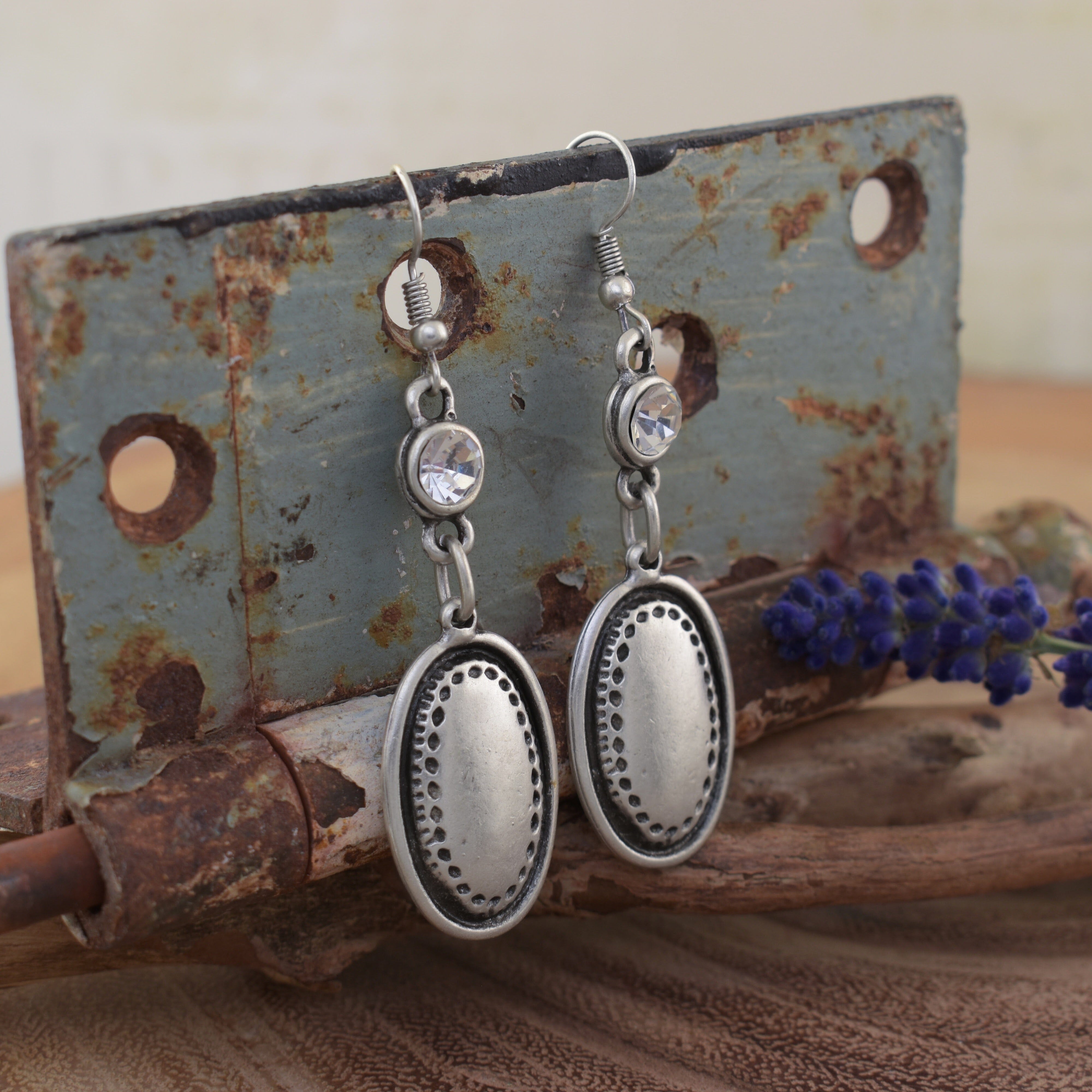 A pair of dangly silver-plated zamak earrings, featuring a large oval and round CZ stone hanging from the hook