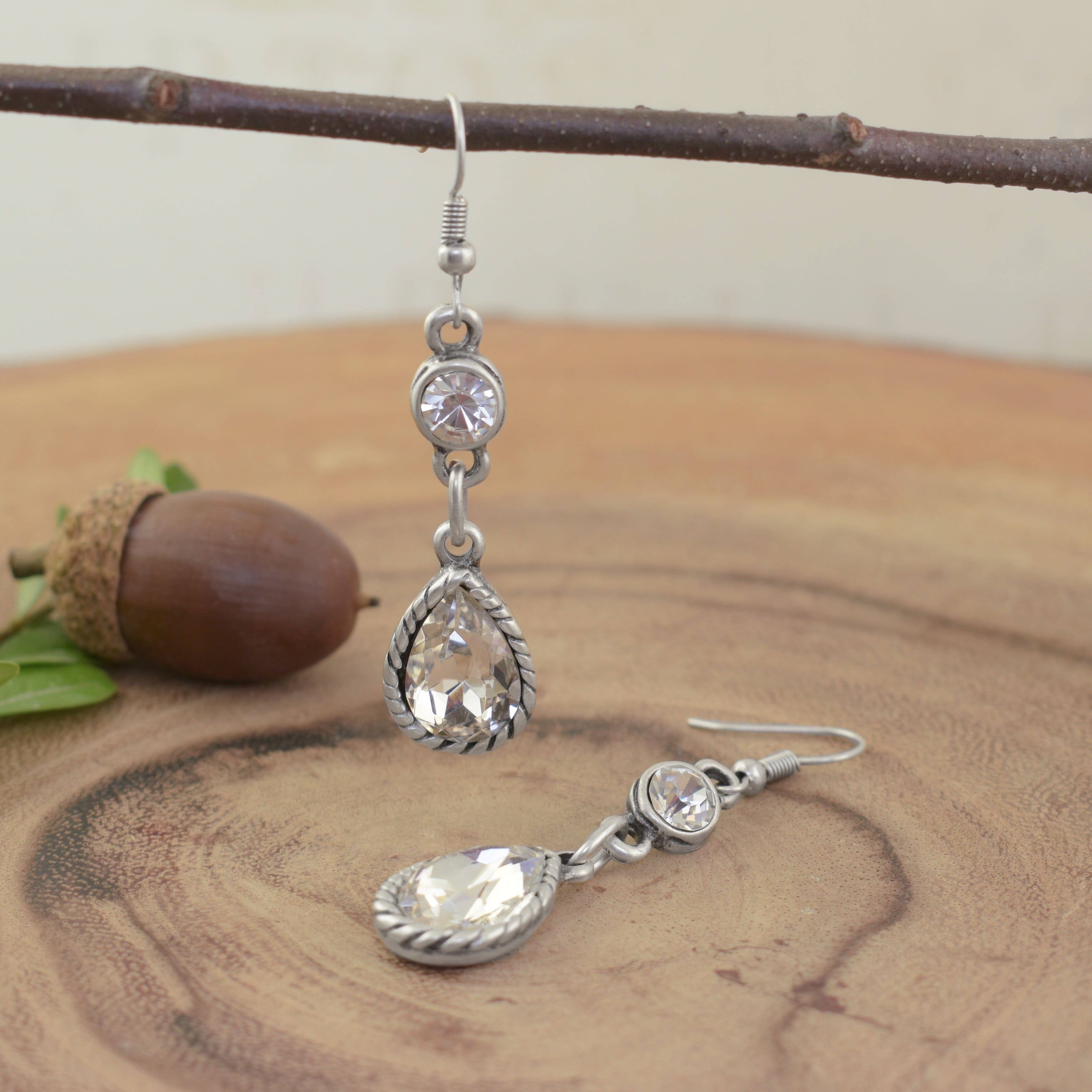 A pair of silver-plated dangly earrings, featuring a round clear CZ and a pear-shaped clear CZ dangling from the end
