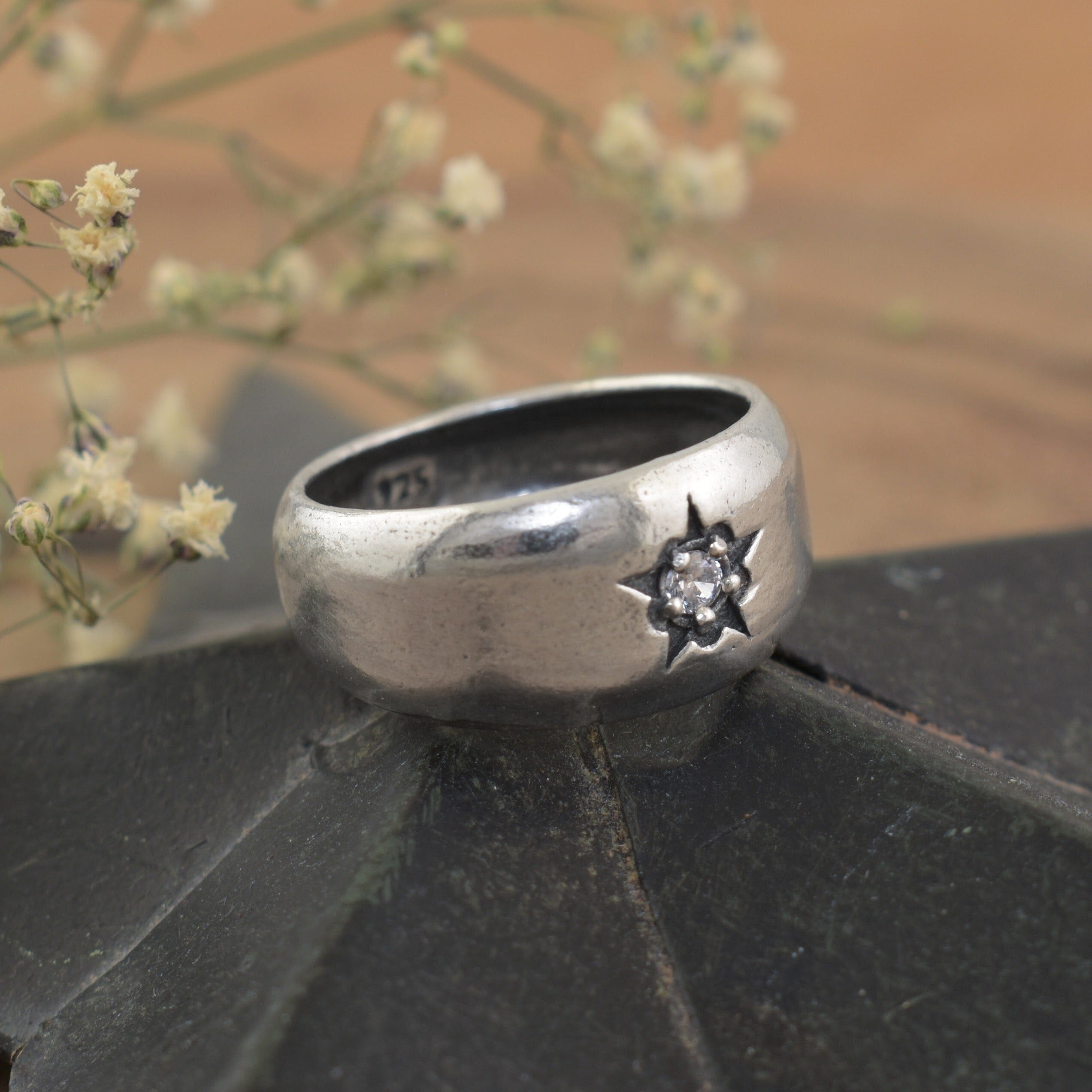 A sterling silver ring featuring a small clear CZ in the center of a starburst design