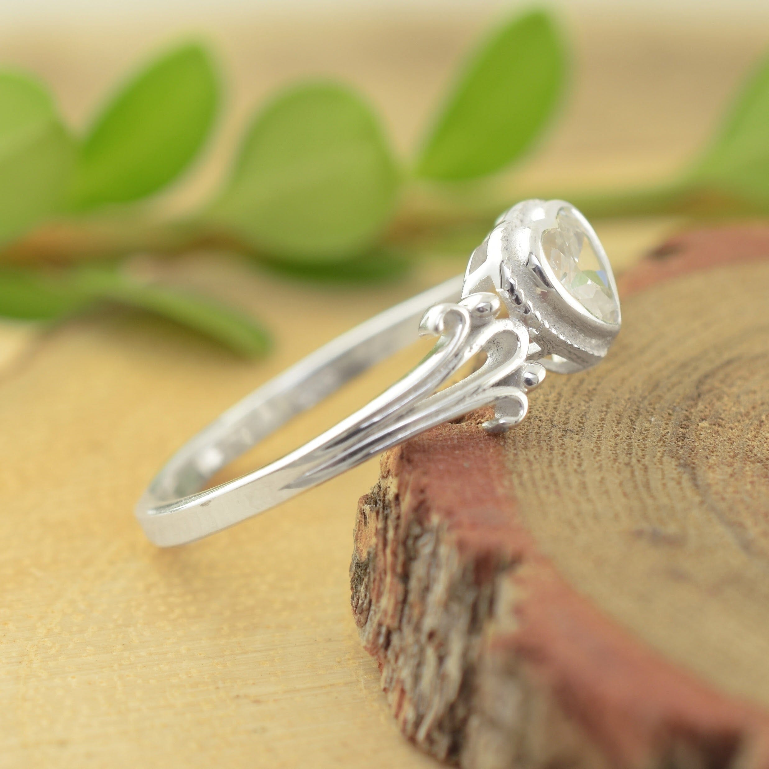 A sterling silver ring with a decorative scrollwork band and a heart-shaped clear gemstone