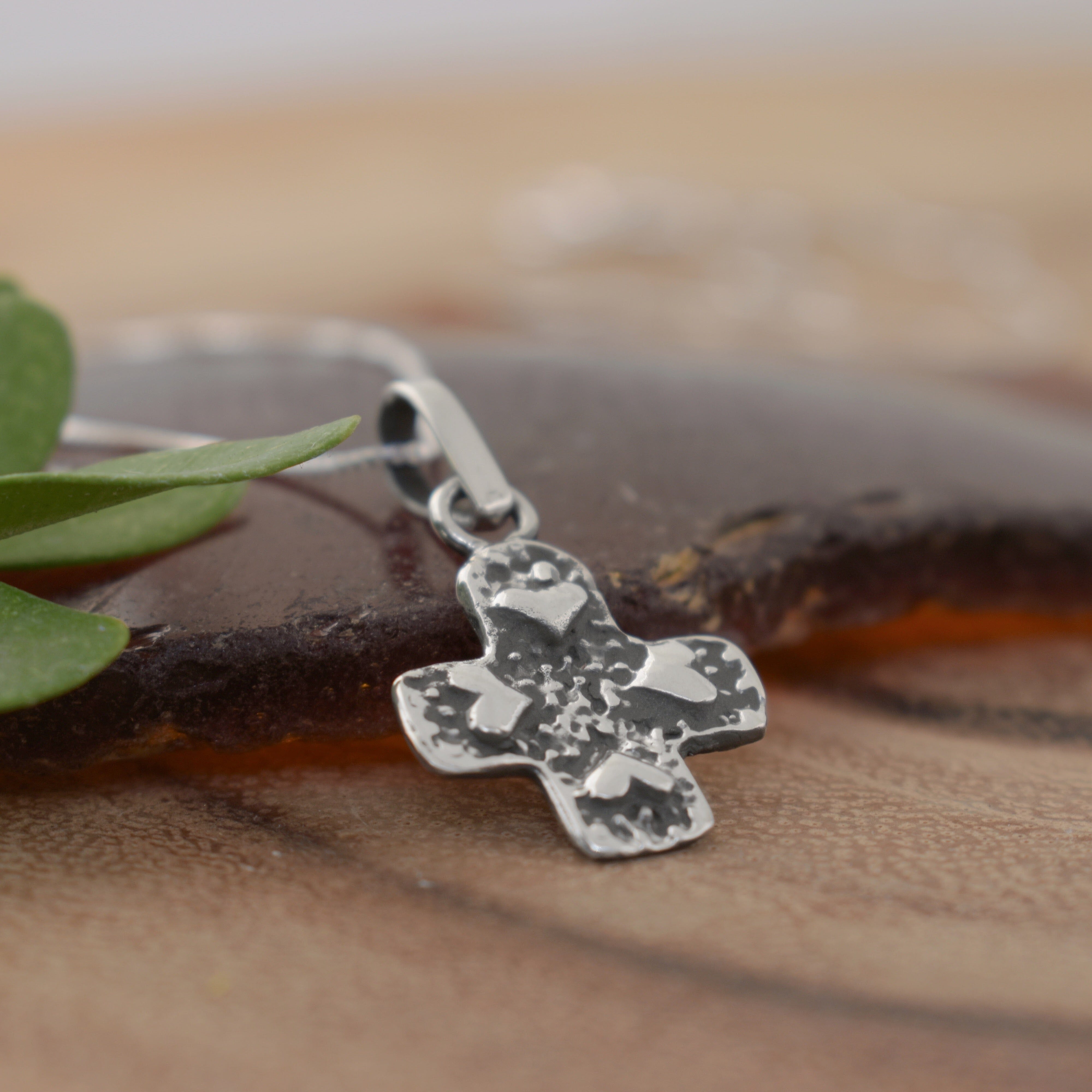 A sterling silver necklace featuring a textured cross pendant with raised heart details