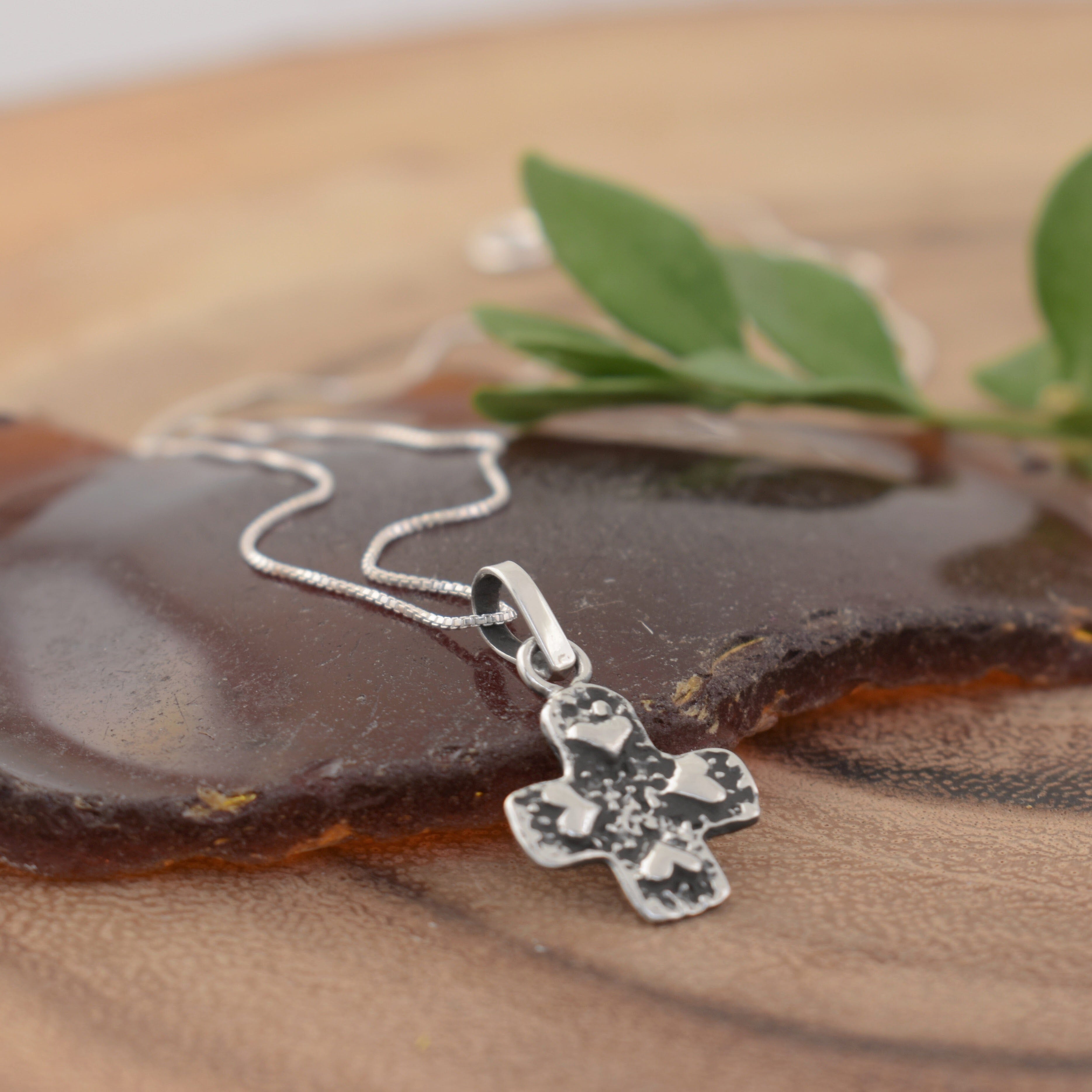 A sterling silver necklace with a cross pendant with raised heart details