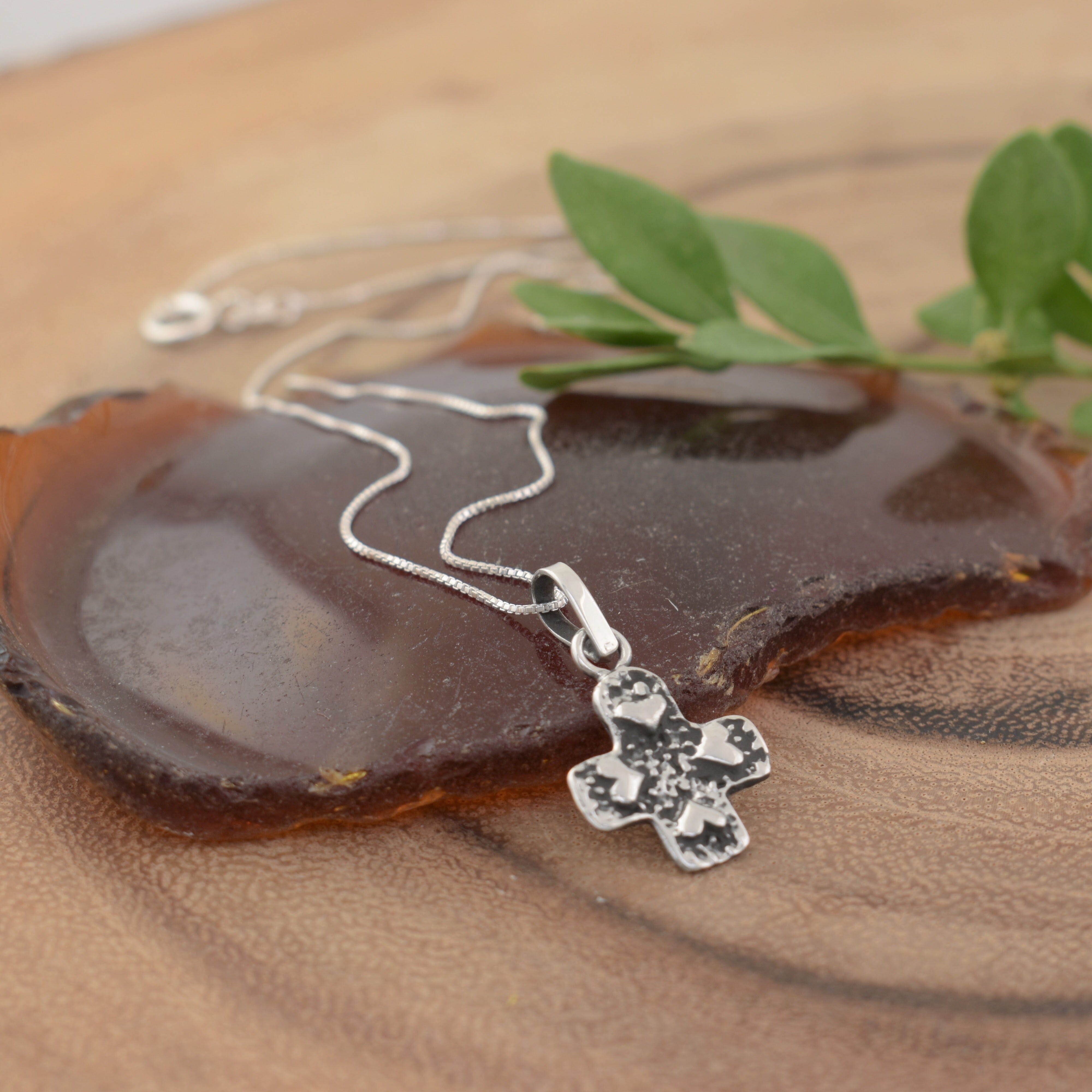 A sterling silver necklace with a textured cross pendant featuring raised heart details