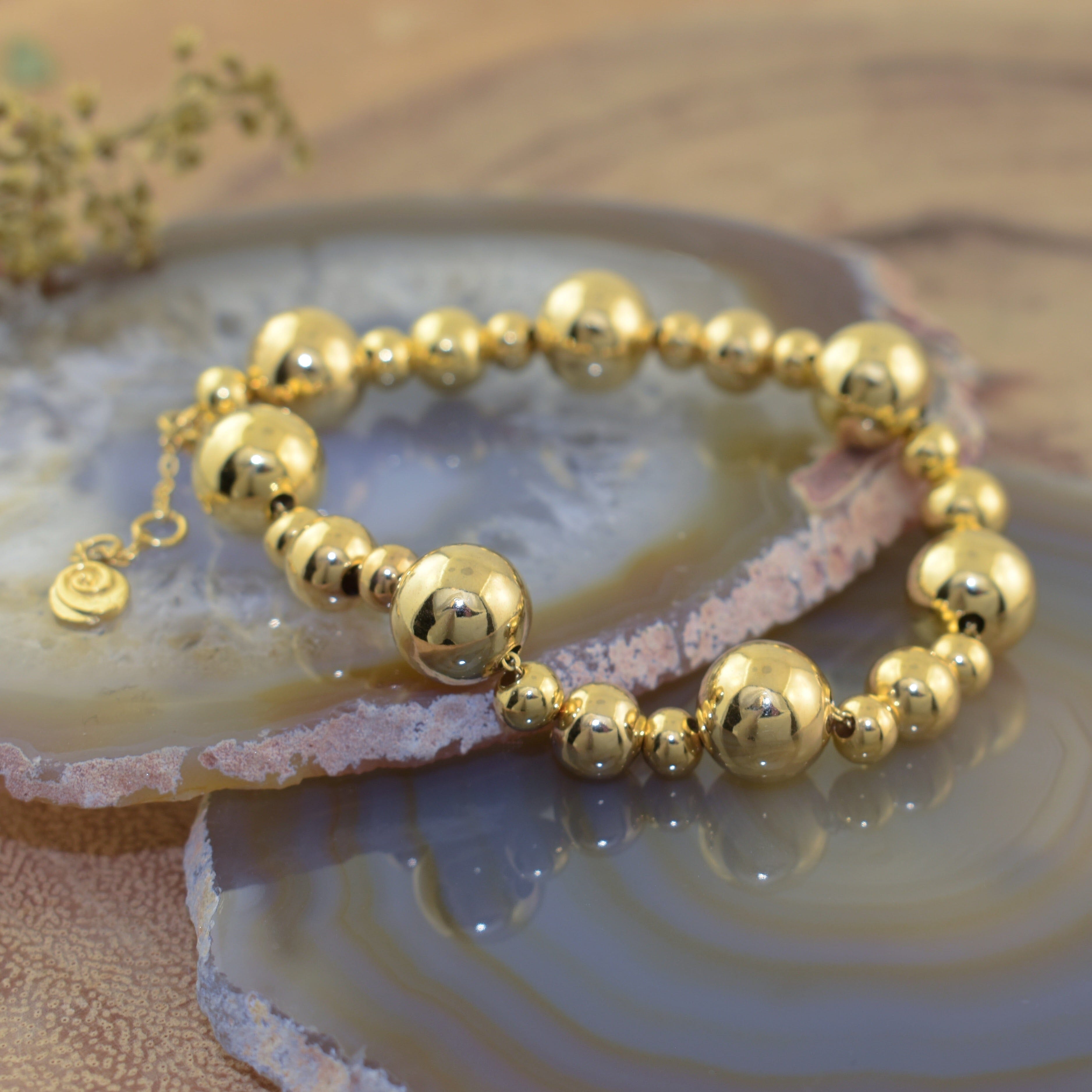 a gold-plated brass beaded bracelet with alternating large and small highly polished round beads with a dangly logo charm