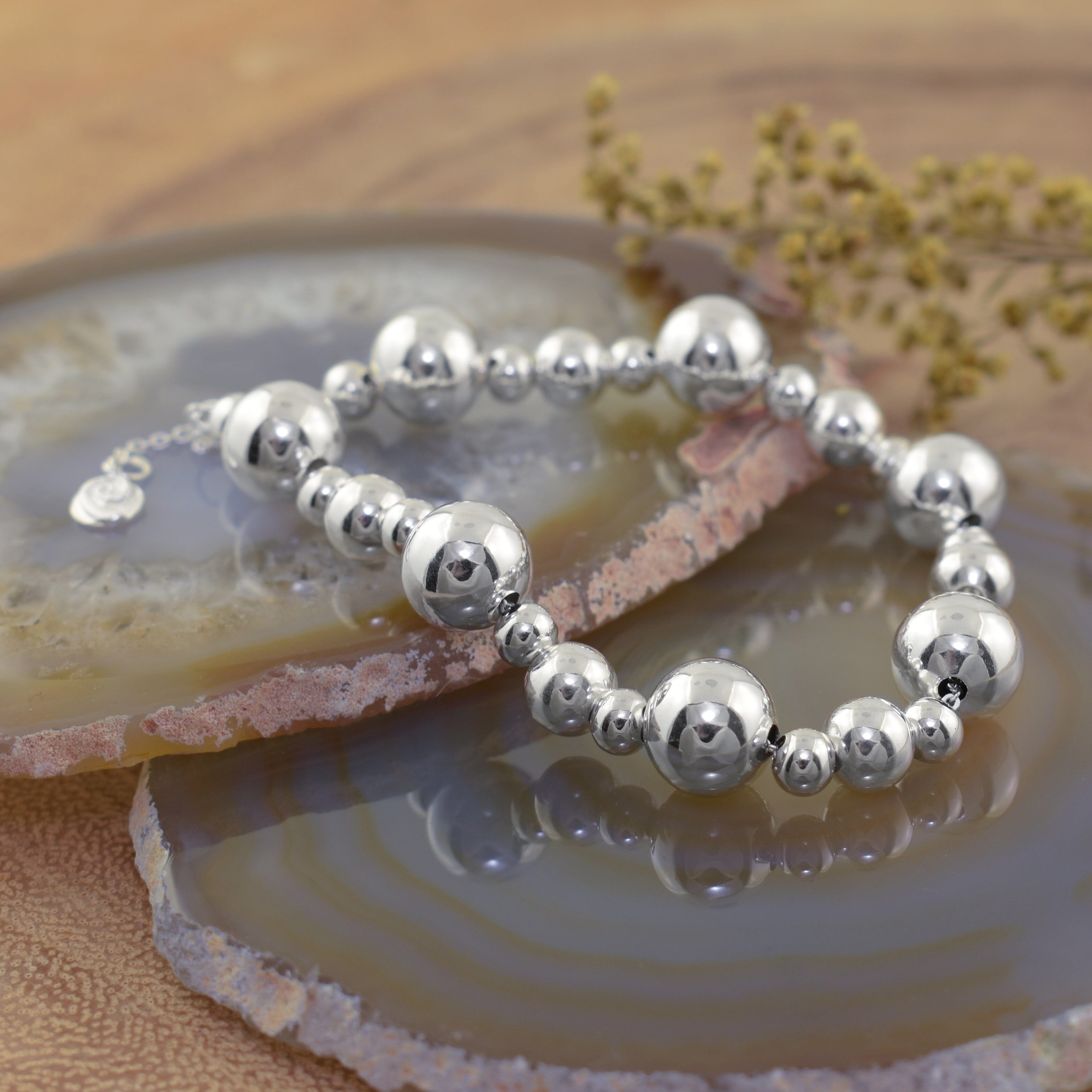 a silver-plated brass beaded bracelet with highly polished round beads and a small dangling logo charm