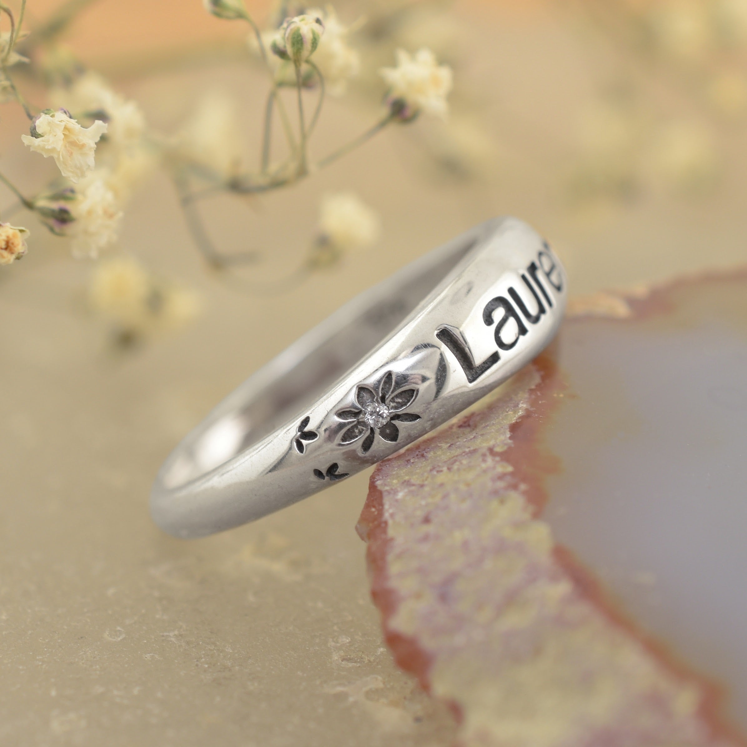 A highly polished sterling silver ring, featuring the name "Lauren" engraved with flower accents bracketing both sides