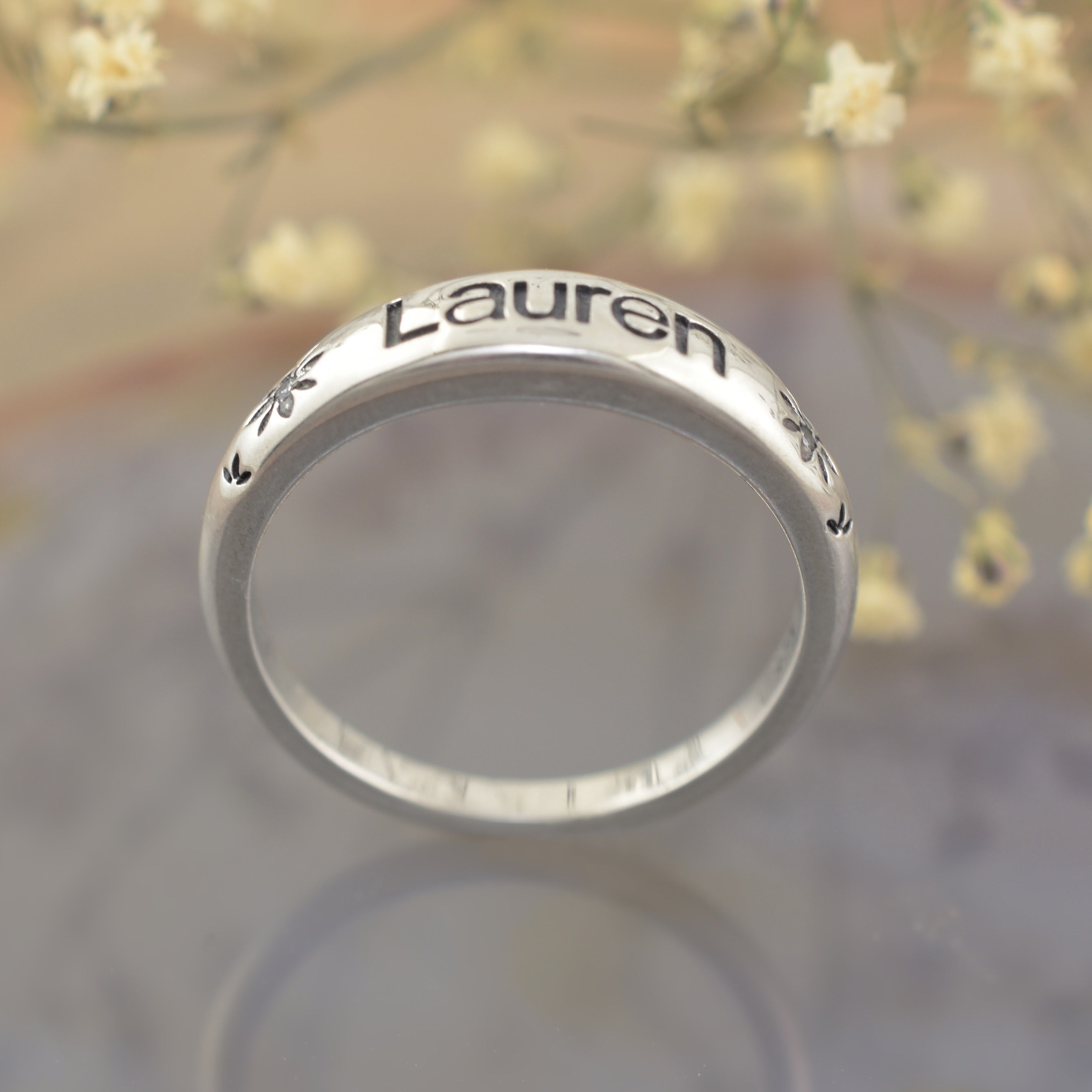 A highly polished sterling silver ring, featuring the name "Lauren" engraved with flower accents bracketing both sides