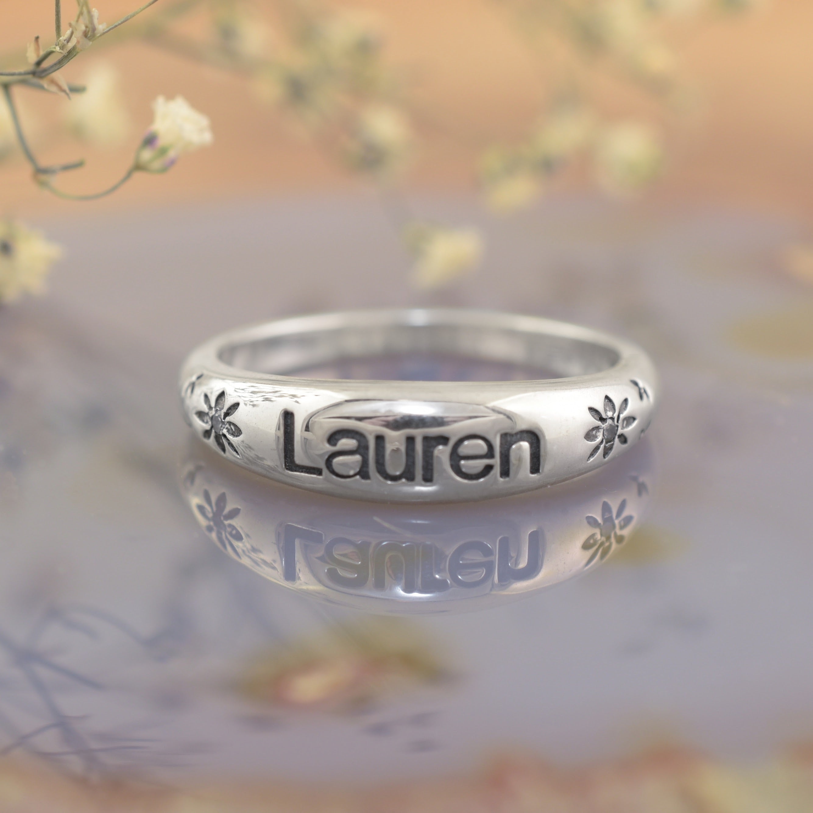 A highly polished sterling silver ring, featuring the name "Lauren" engraved with flower accents bracketing both sides