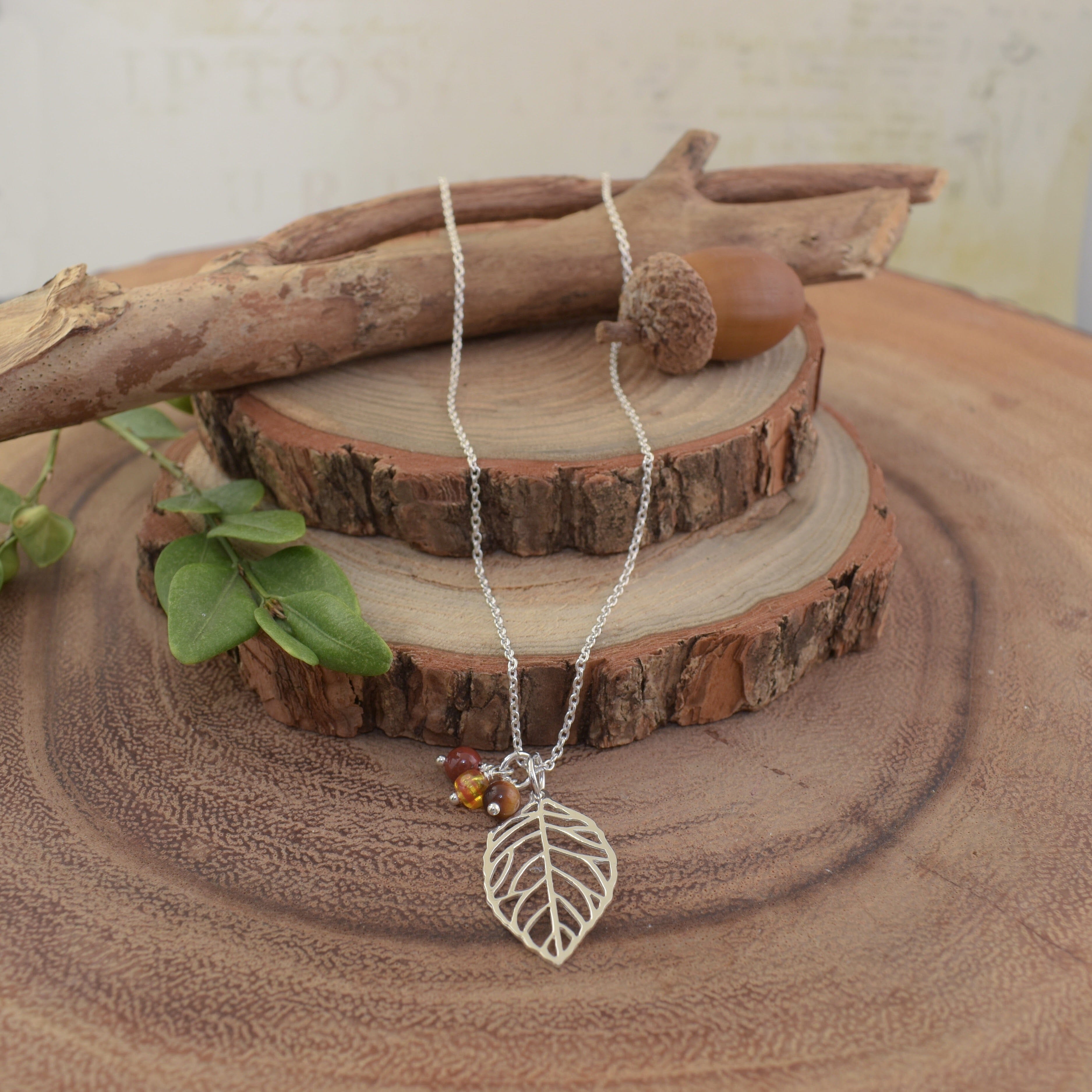 A sterling silver necklace featuring a silver leaf pendant and 3 small beads in various fall colors