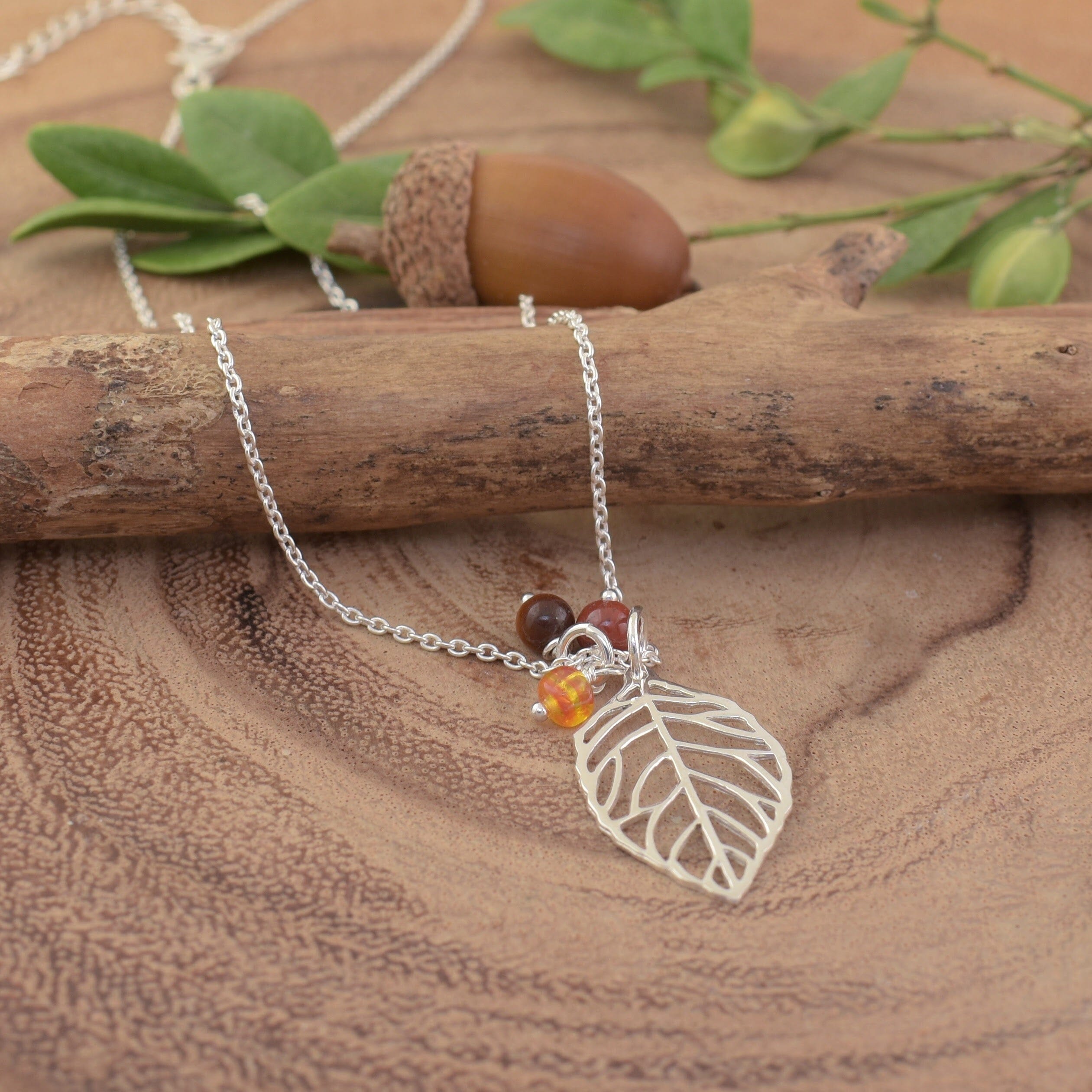 A sterling silver necklace featuring a silver leaf pendant and 3 small beads in various fall colors