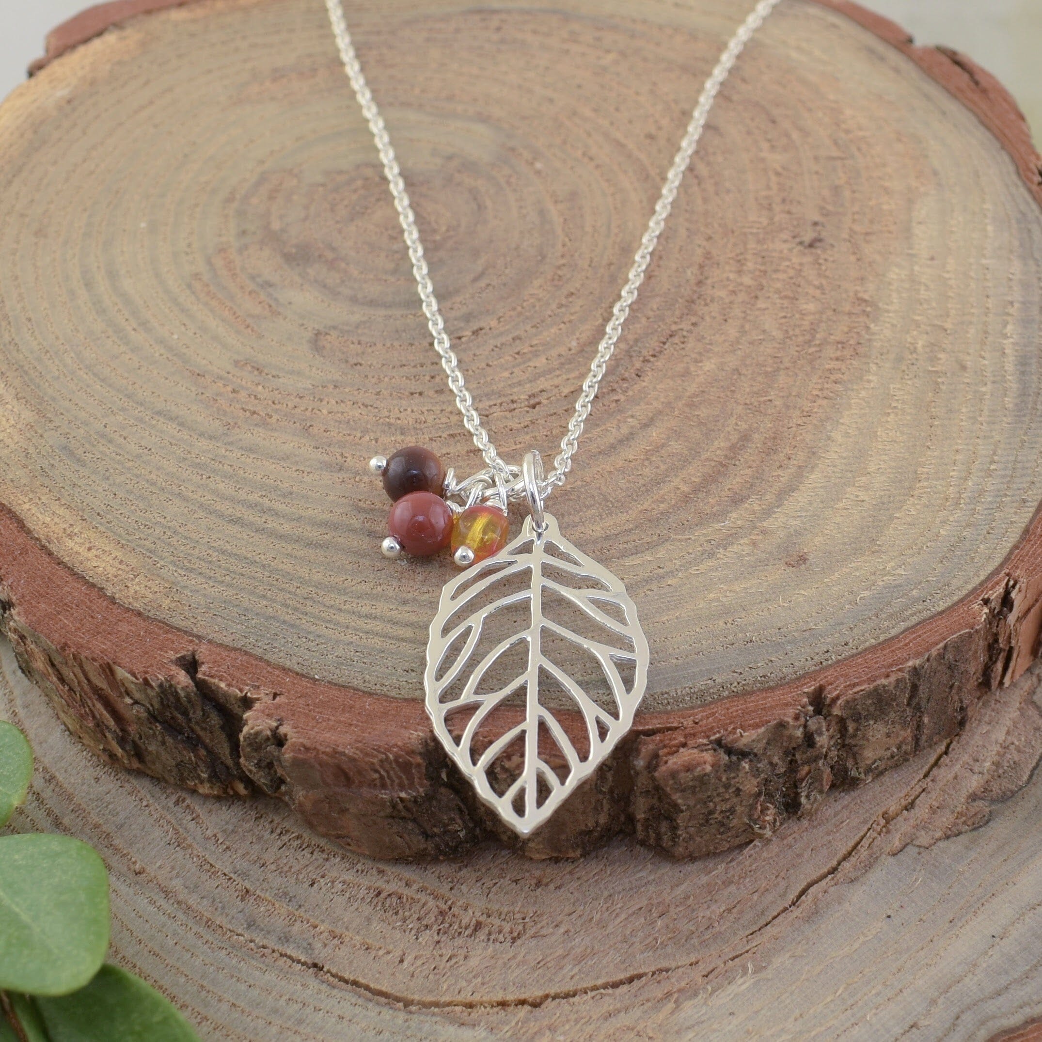 A sterling silver necklace featuring a silver leaf pendant and 3 small beads in various fall colors