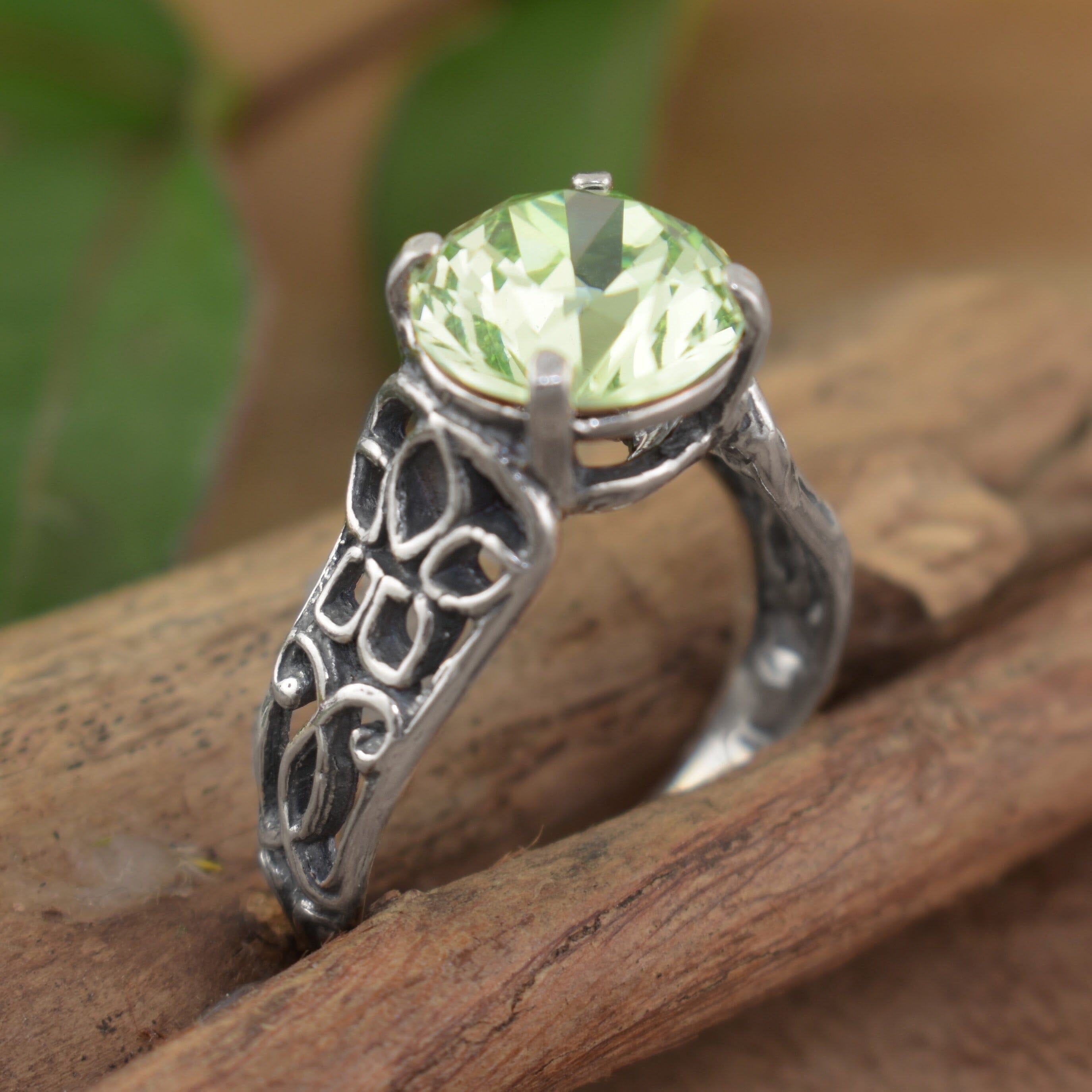 a silver ring with an ornate filigree band and a large round-cut light green gemstone