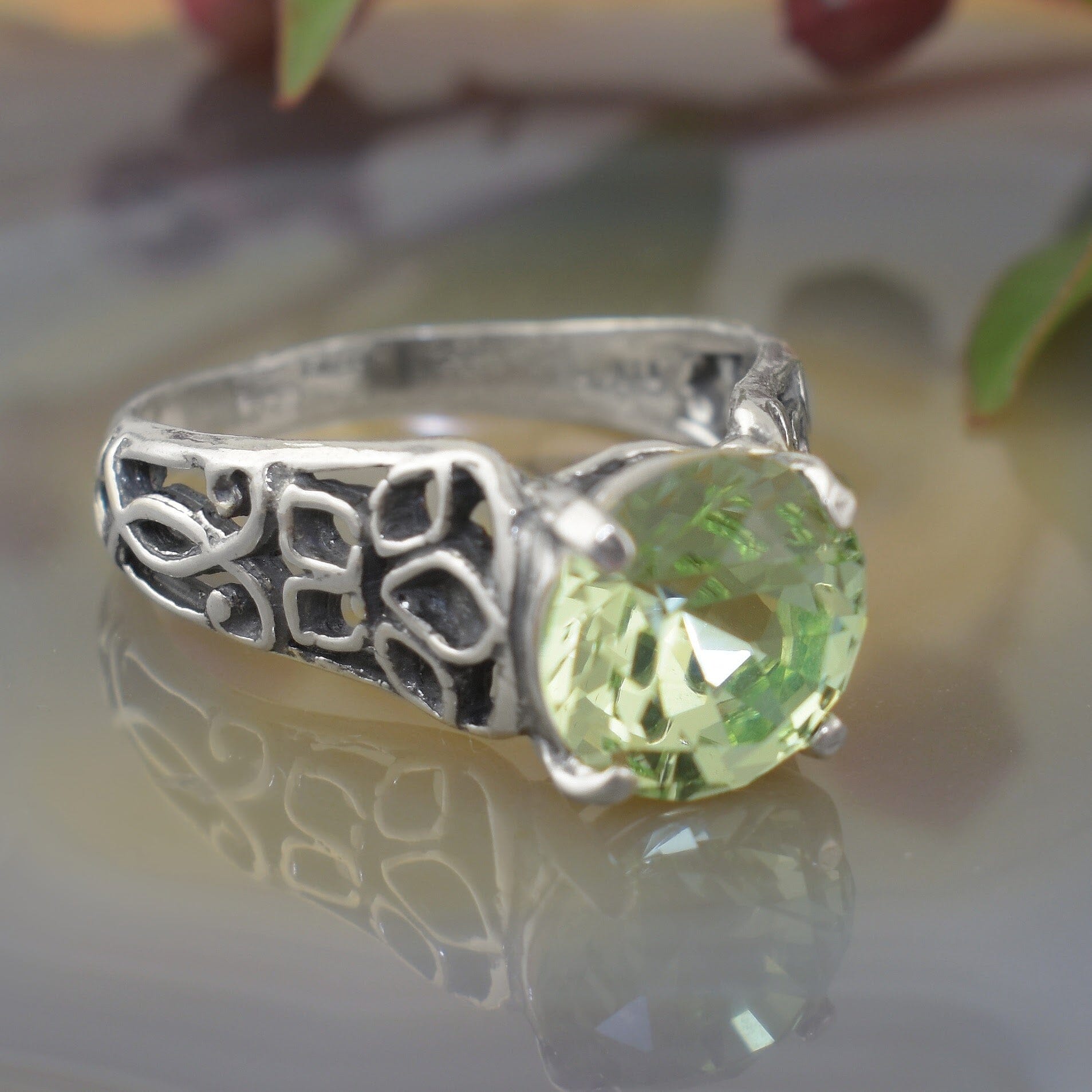a silver ring with an ornate filigree band and a large round light green gemstone