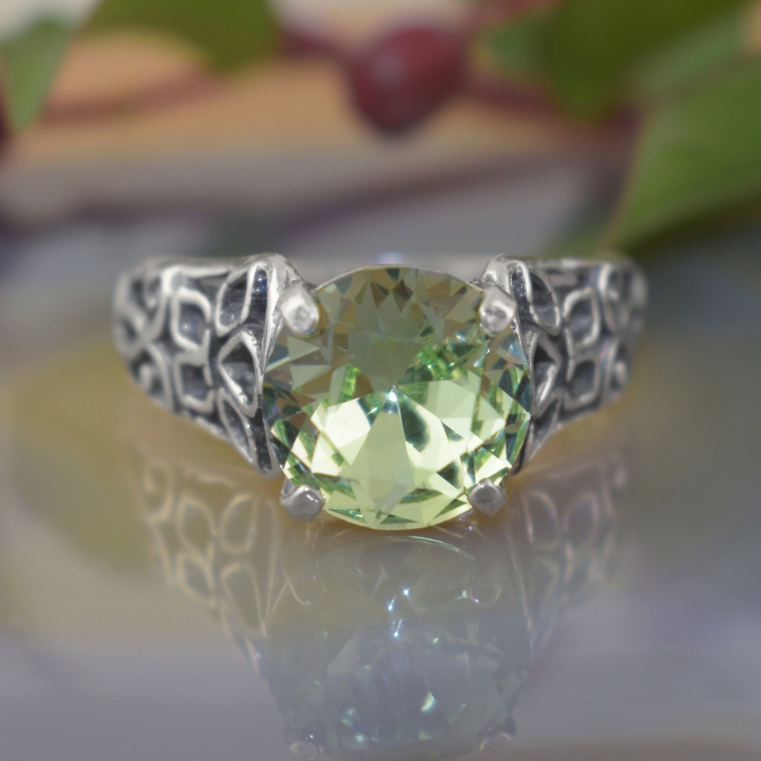 a silver ring with an ornate filigree band and a large round-cut light green gemstone