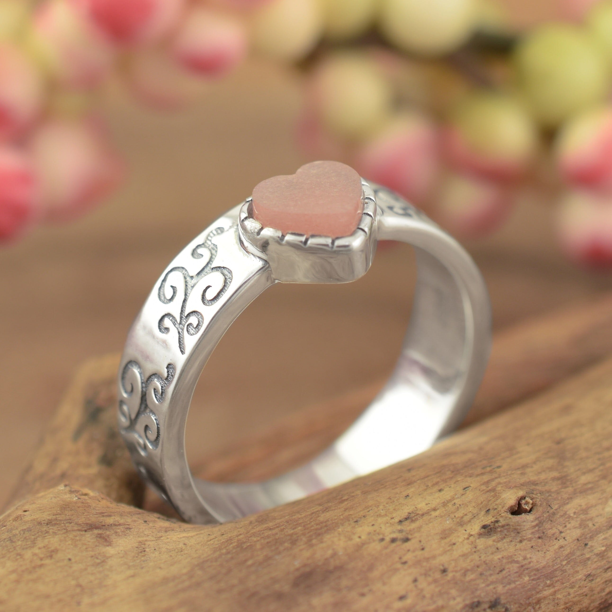 A high-polished sterling silver ring with engraved filigree along the band, featuring a pale salmon-colored heart
