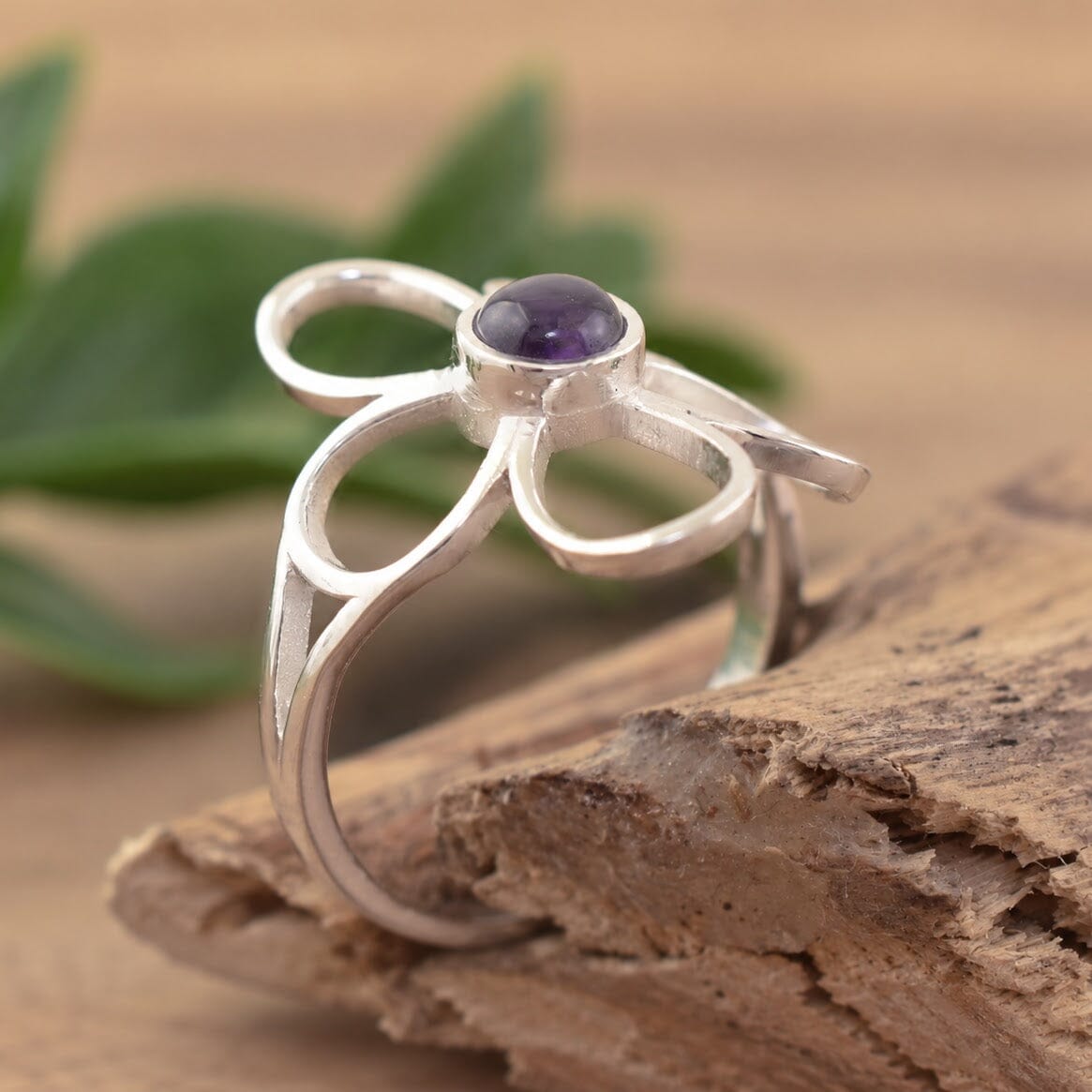 A sterling silver ring with an organic flower-shaped design with cutouts in the petals and an amethyst stone in the center