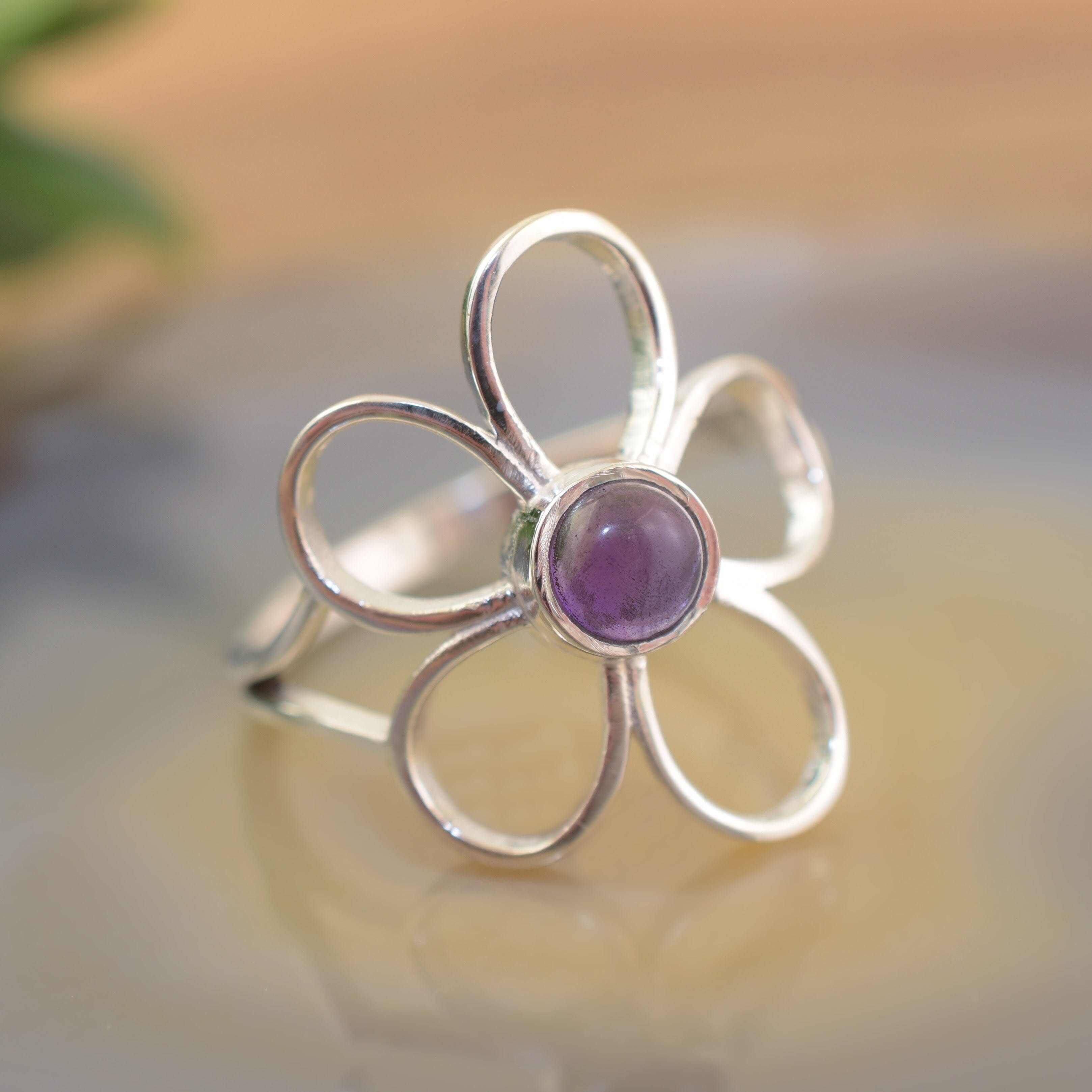 A sterling silver ring with a large organic flower-shaped design with cutouts in the petals and an amethyst stone in the center