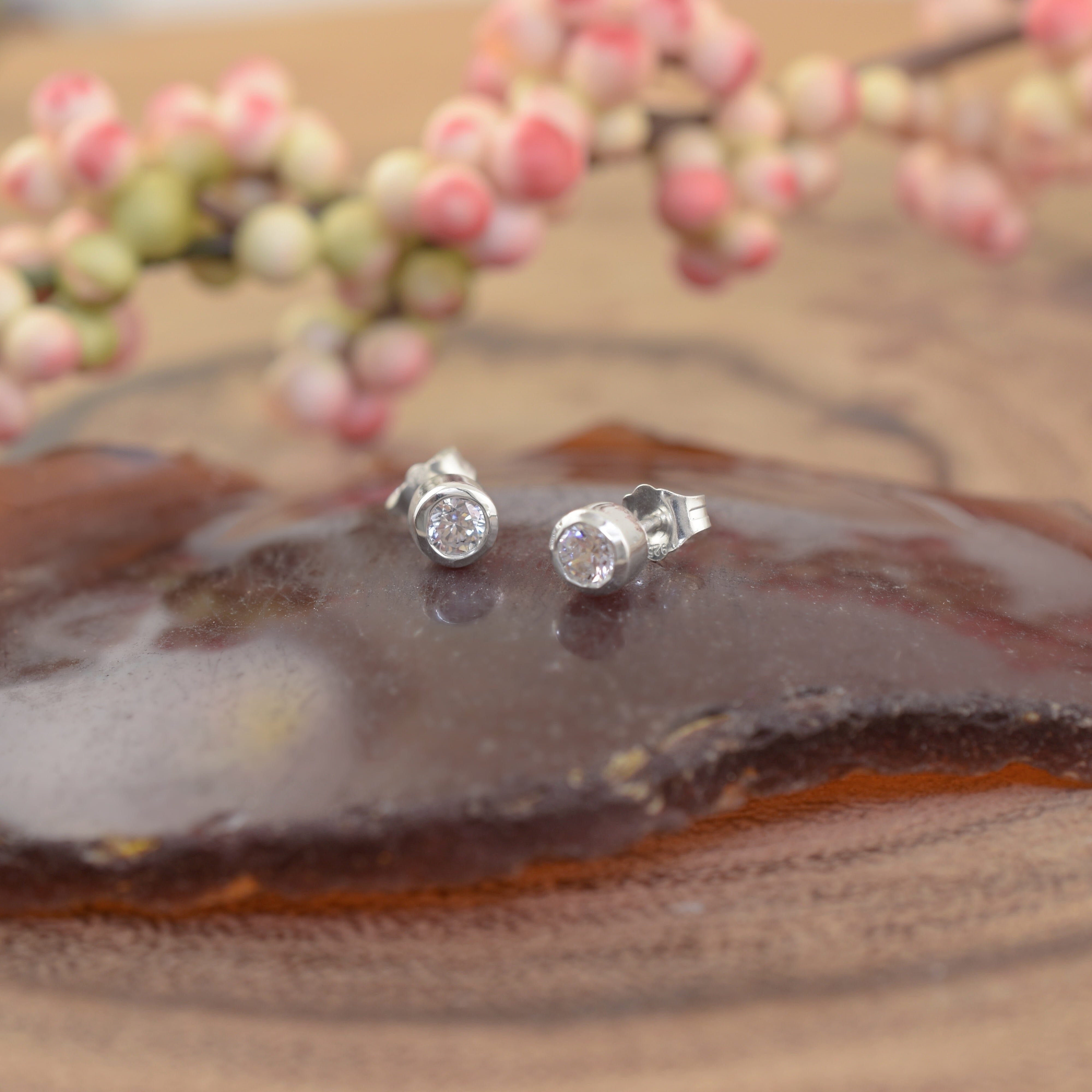 A small pair of high-polished post earrings, featuring a round clear CZ