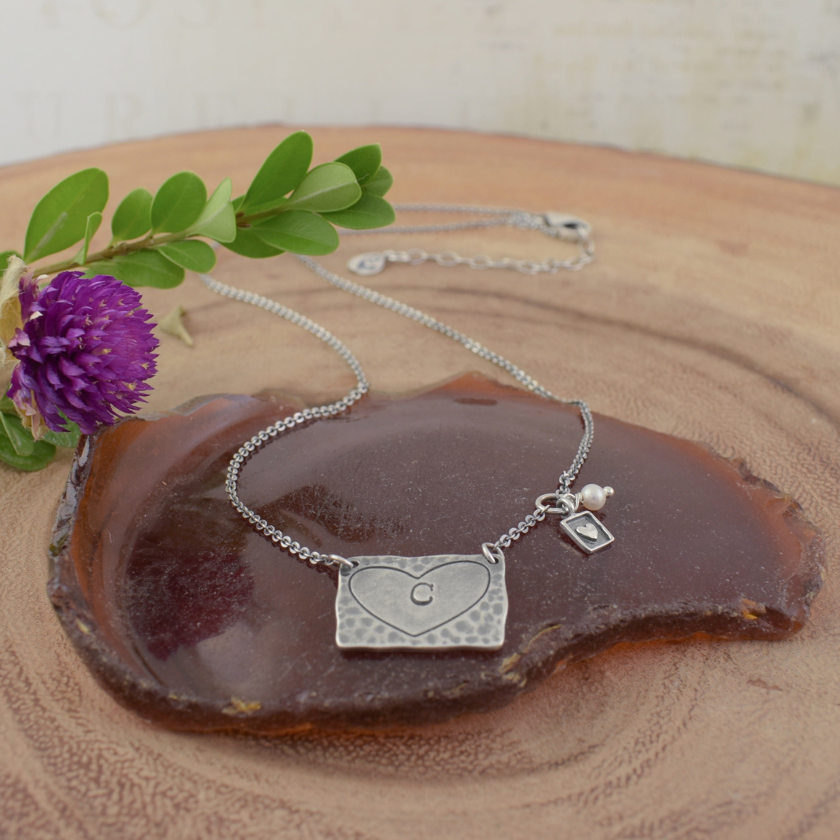 A sterling silver heart-shaped pendant necklace with a small initial 'C' engraved in the center