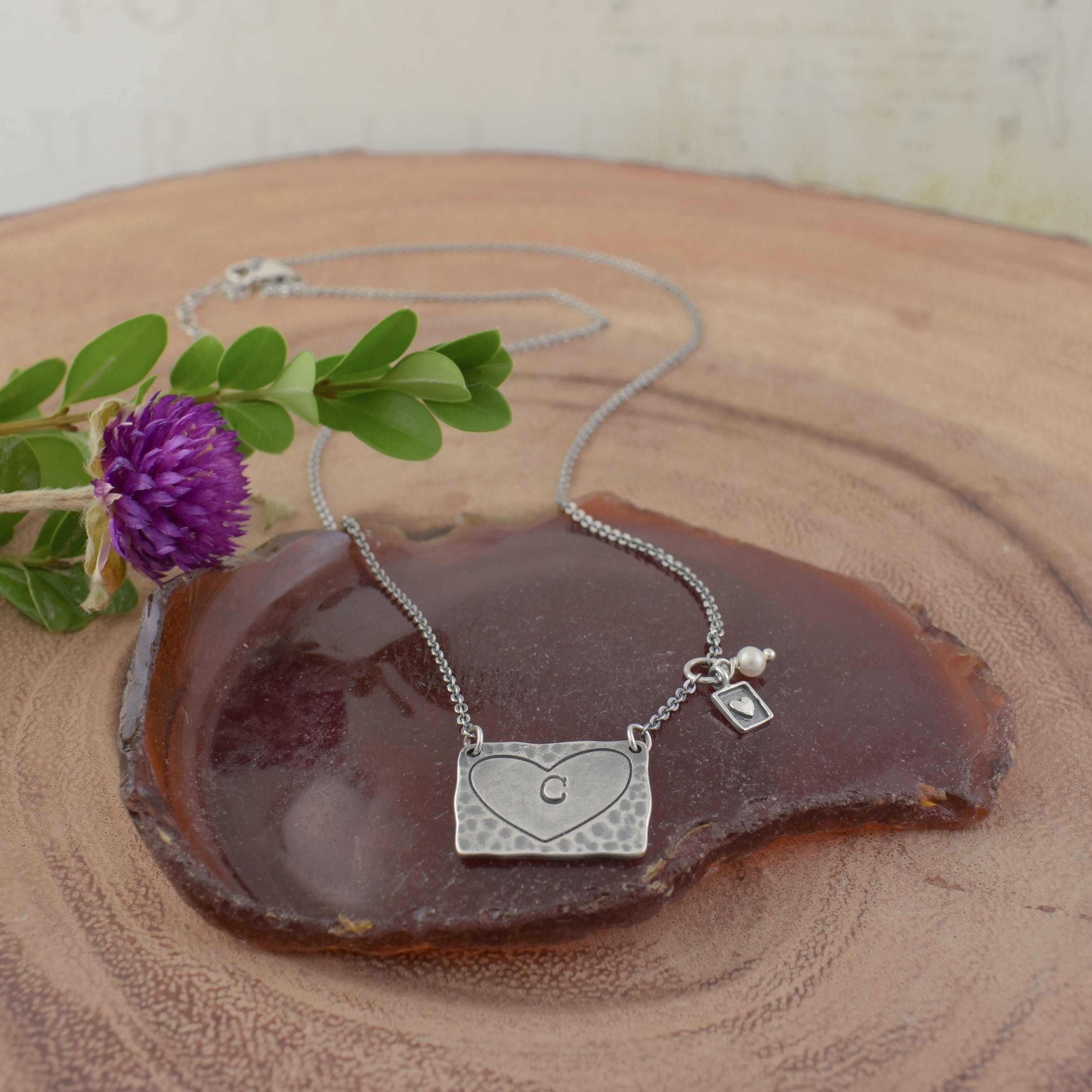 A sterling silver heart-shaped pendant necklace with a small initial 'C' engraved in the center